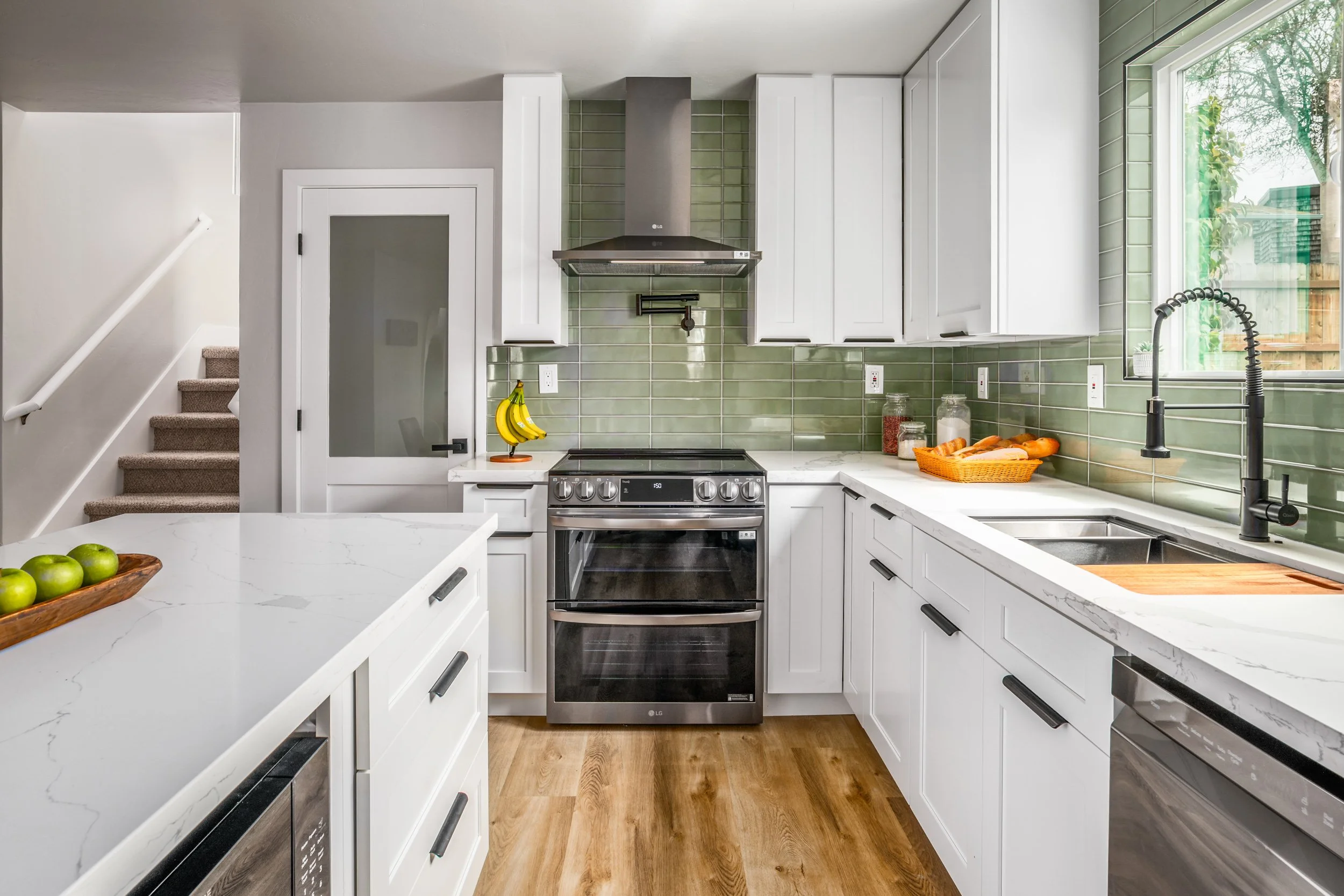Modern kitchen with white shaker cabinets, green subway-tile backsplash, and quartz waterfall island