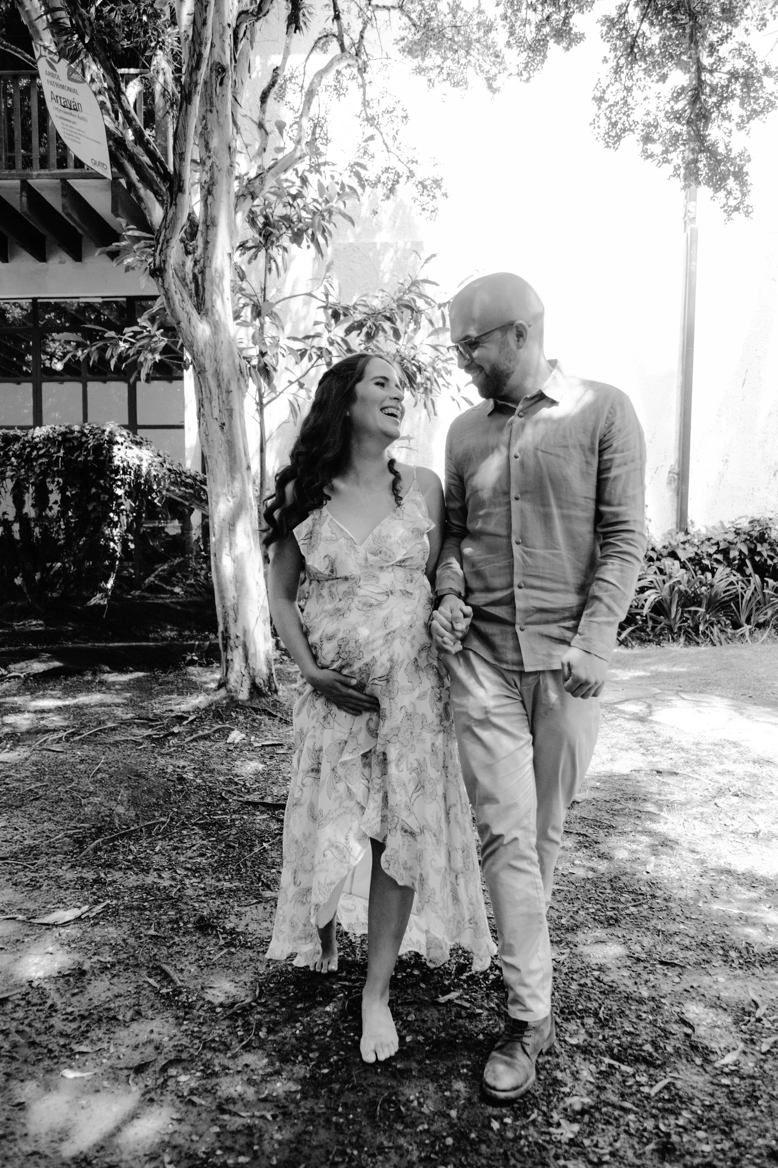 Pareja feliz caminando juntos por un parque, la mujer está embarazada y ambos se miran sonrientes.