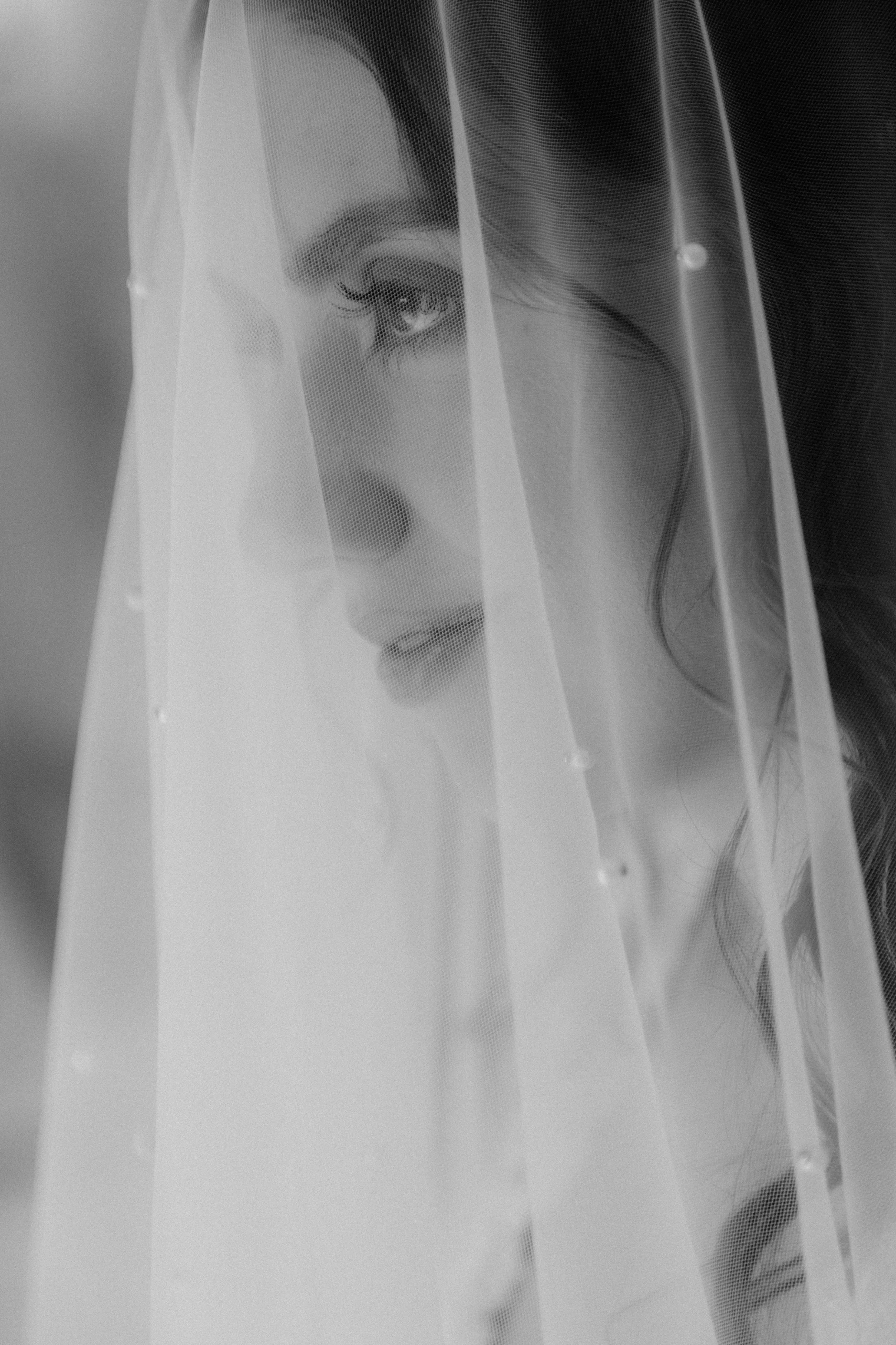 Retrato en blanco y negro de una mujer con velo transparente cubriéndola parcialmente, mirando pensativa.