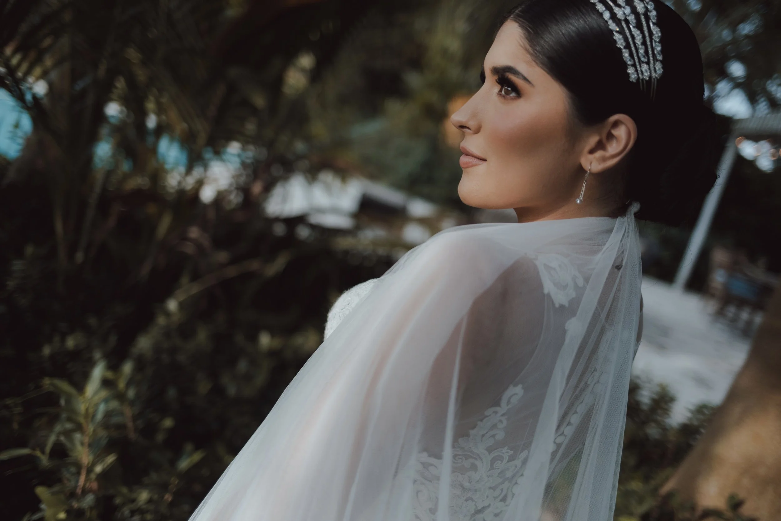 Mujer en vestido de novia con peinado elegante y accesorios, en un entorno natural al aire libre.