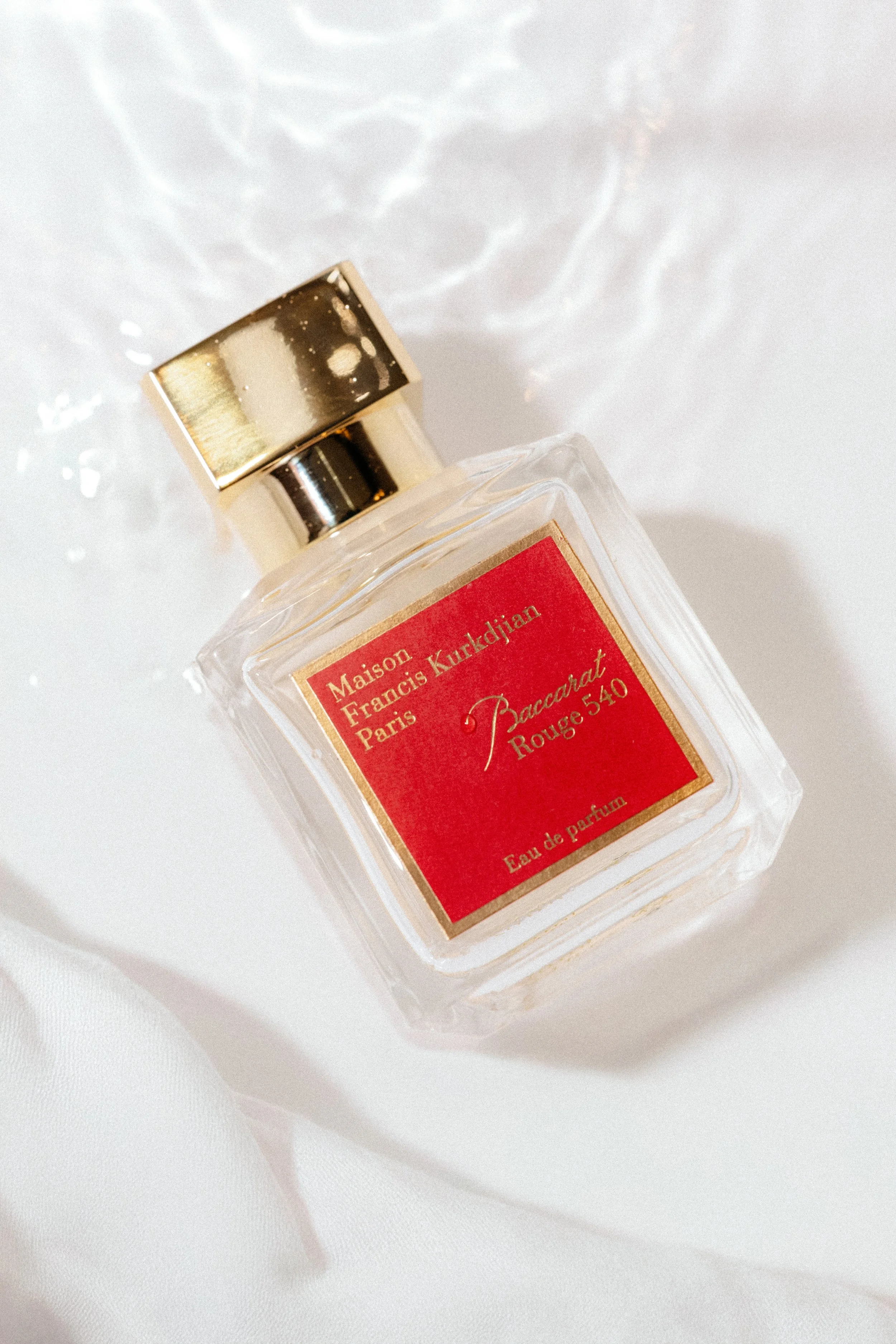 Frasco de perfume con etiqueta roja y letras doradas, sobre fondo blanco.