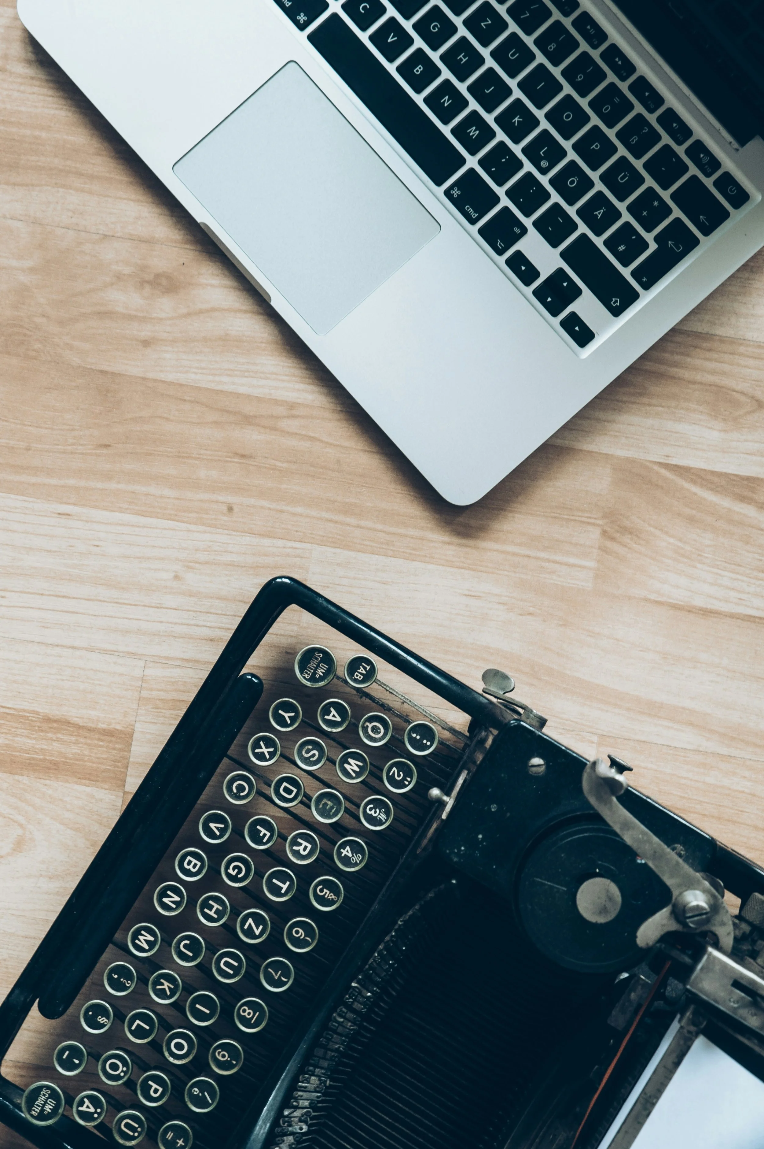 Top view of a vintage typewriter and a modern laptop on a wooden desk.