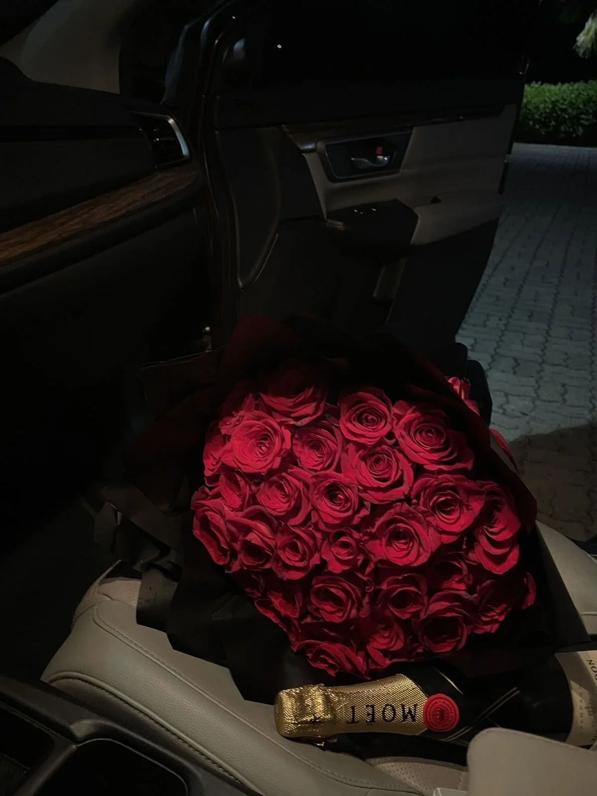 A bouquet of red roses on a car seat with a gold MOLTEN champagne bottle nearby.