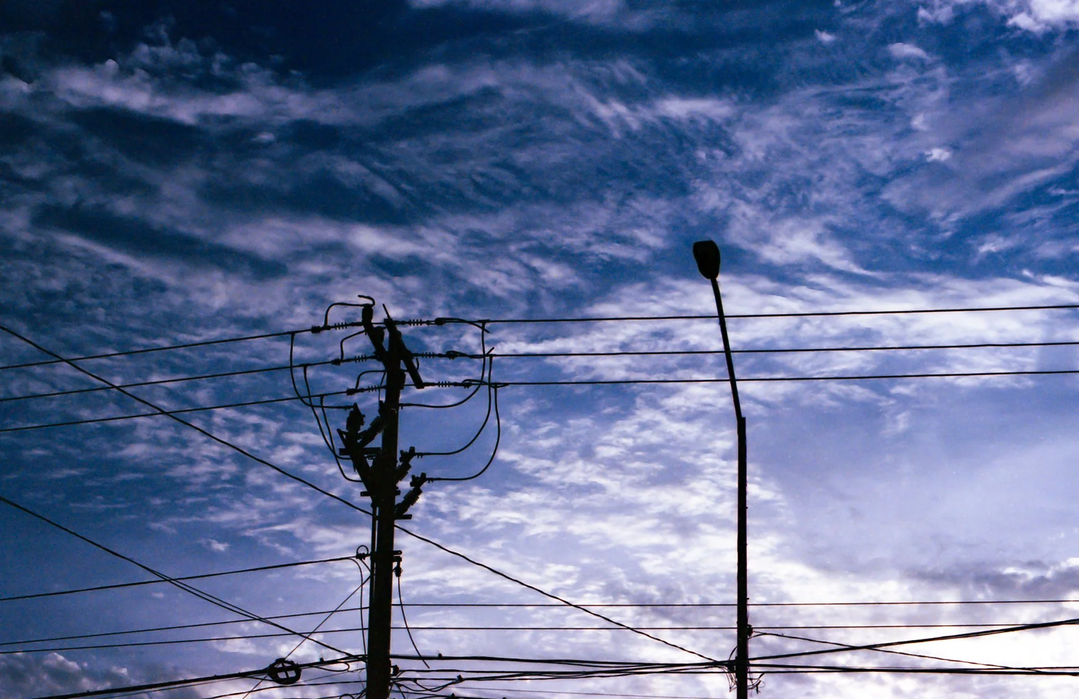 Poste de luz y cables eléctricos en un cielo con nubes y una puesta de sol
