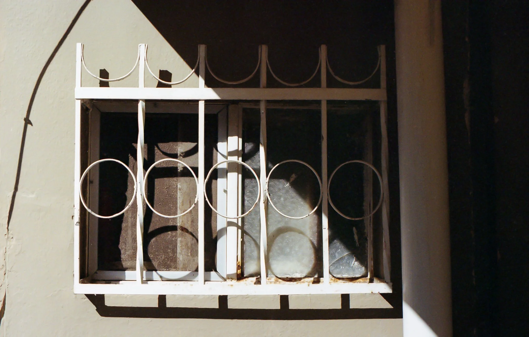 Reja de barrotes blancos en una ventana con sombra en la pared