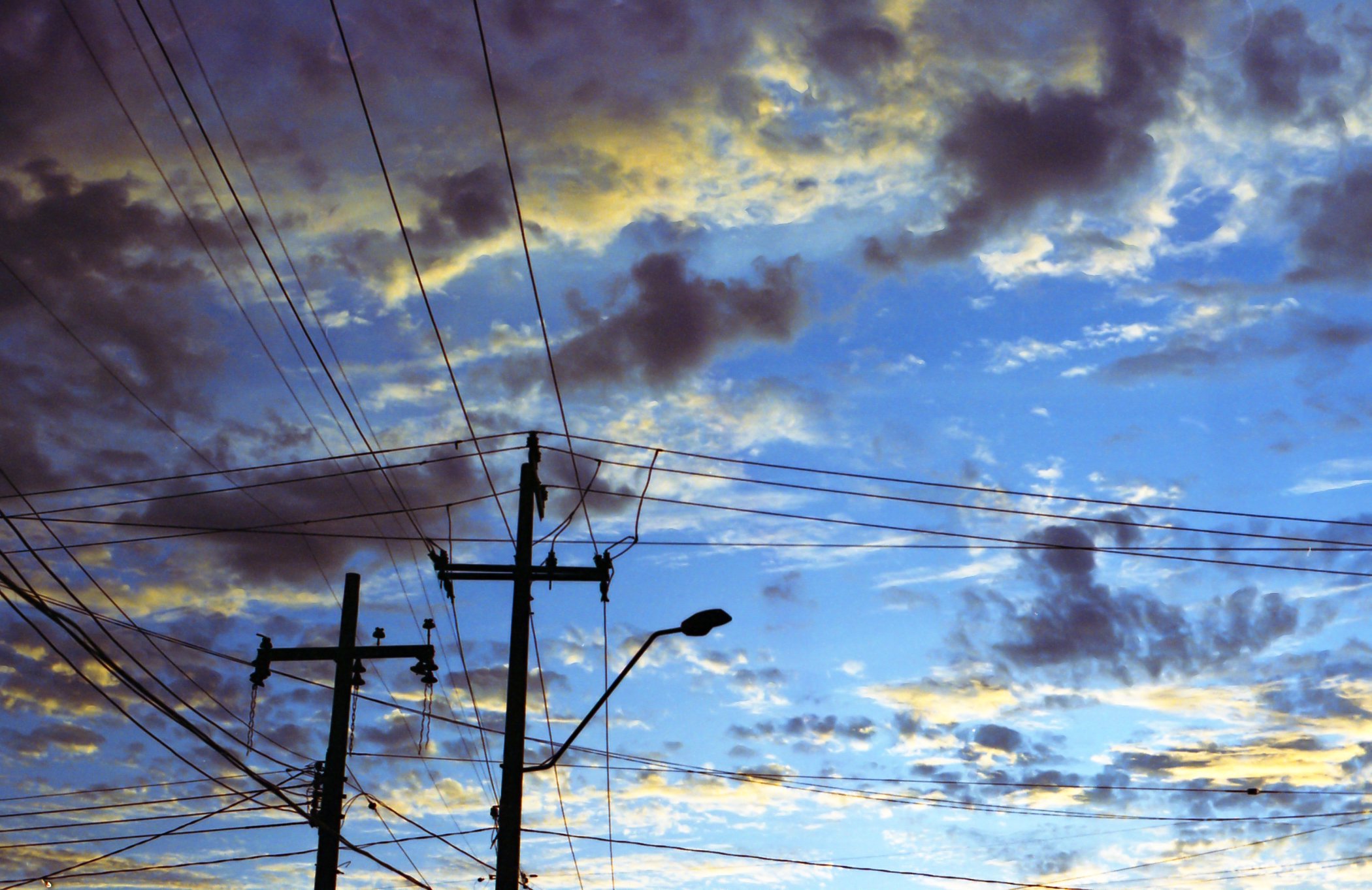 Cielo con nubes y postes de energía eléctrica con cables en primer plano