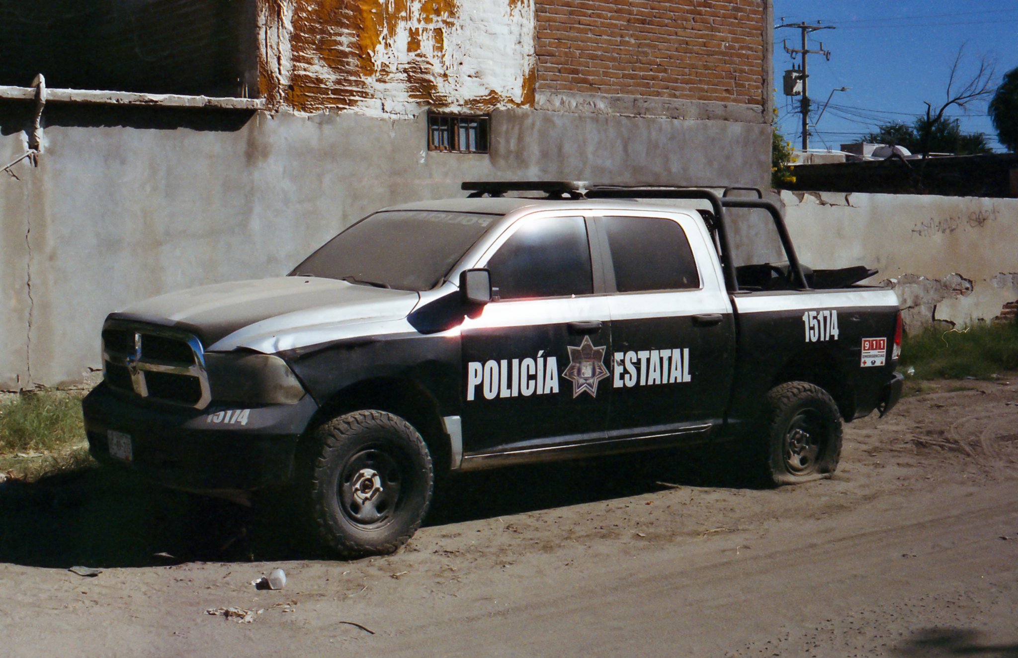 Camión de policía estatal estacionado en una calle con paredes en construcción y cables en el fondo.