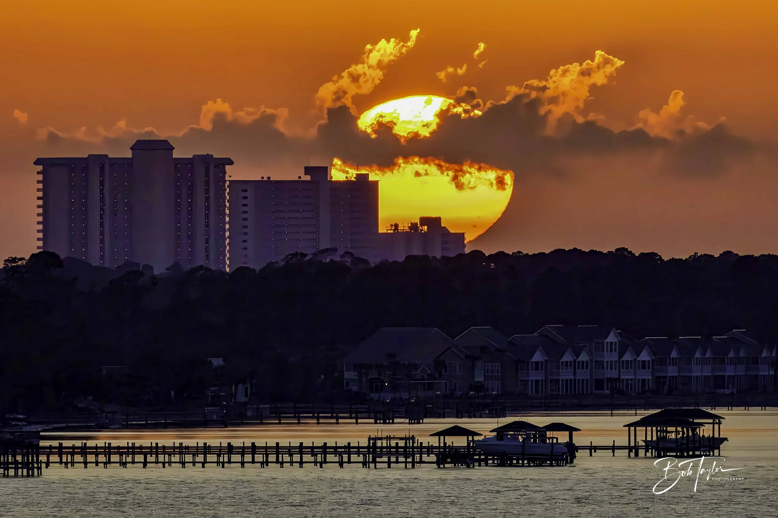 Photo of the sun setting over St Andrews Bay and behind condominiums on Panama City Beach