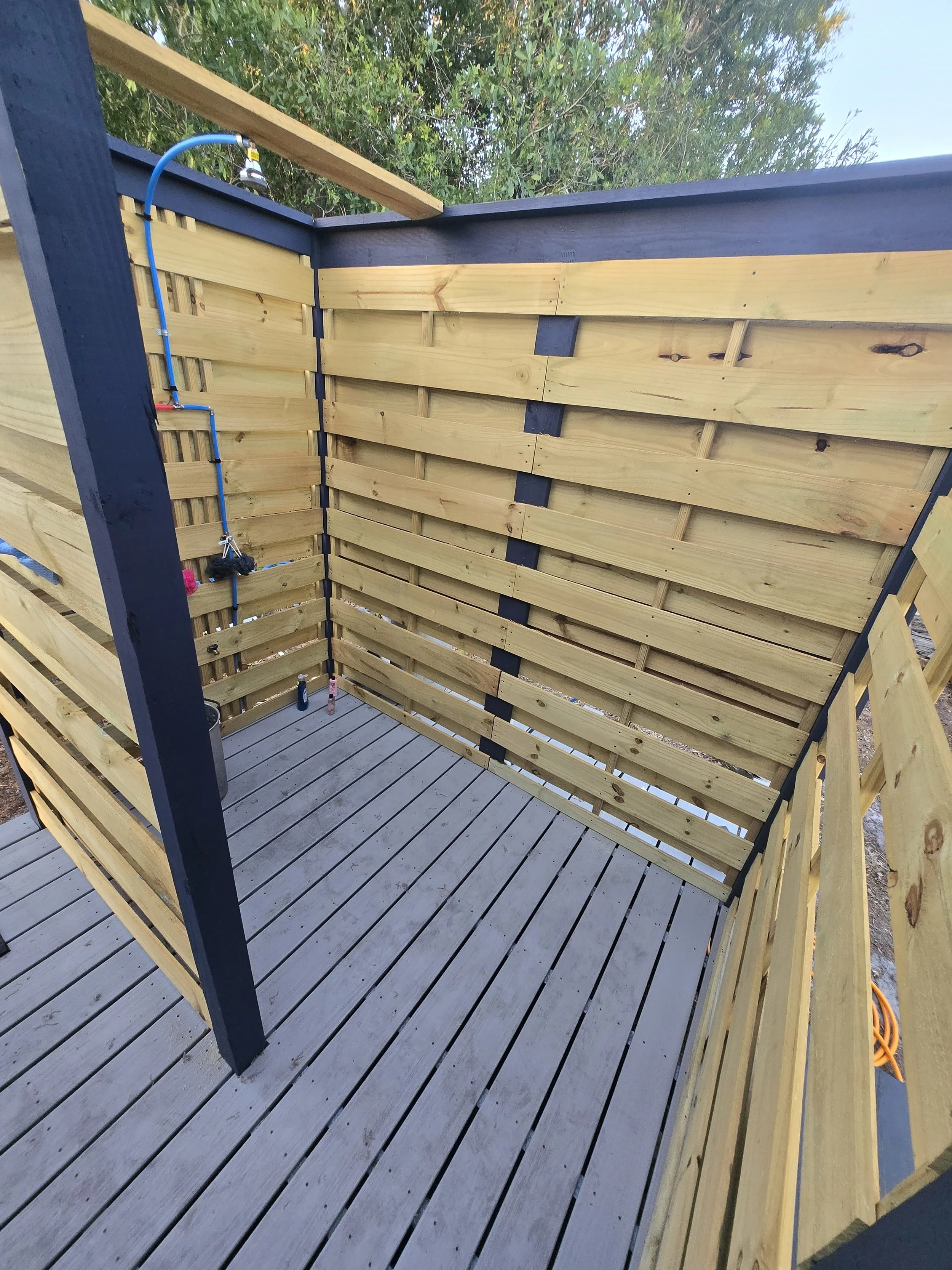 Outdoor shower with wooden enclosure and gray composite deck floor.