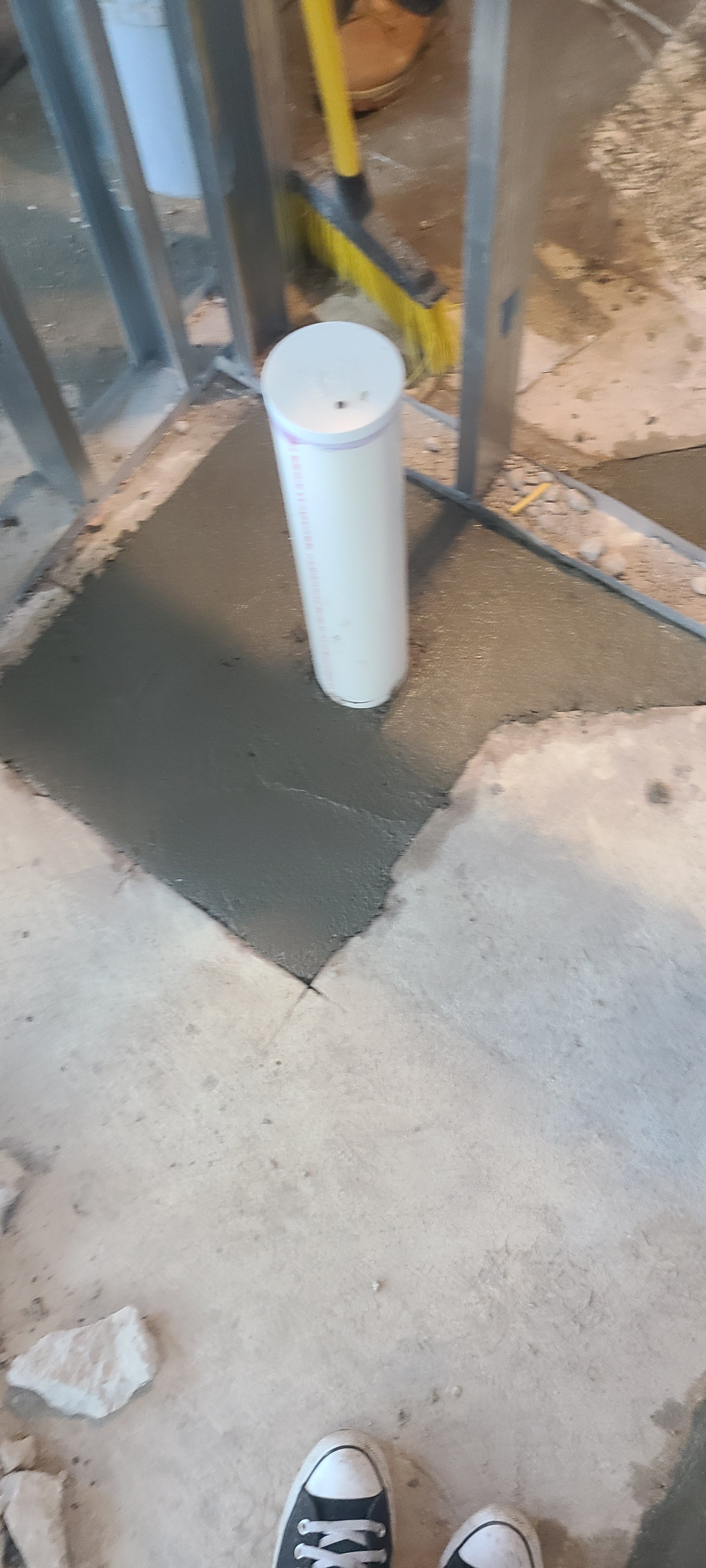 Construction site floor with fresh concrete patch, metal framing, and a drain in the center.