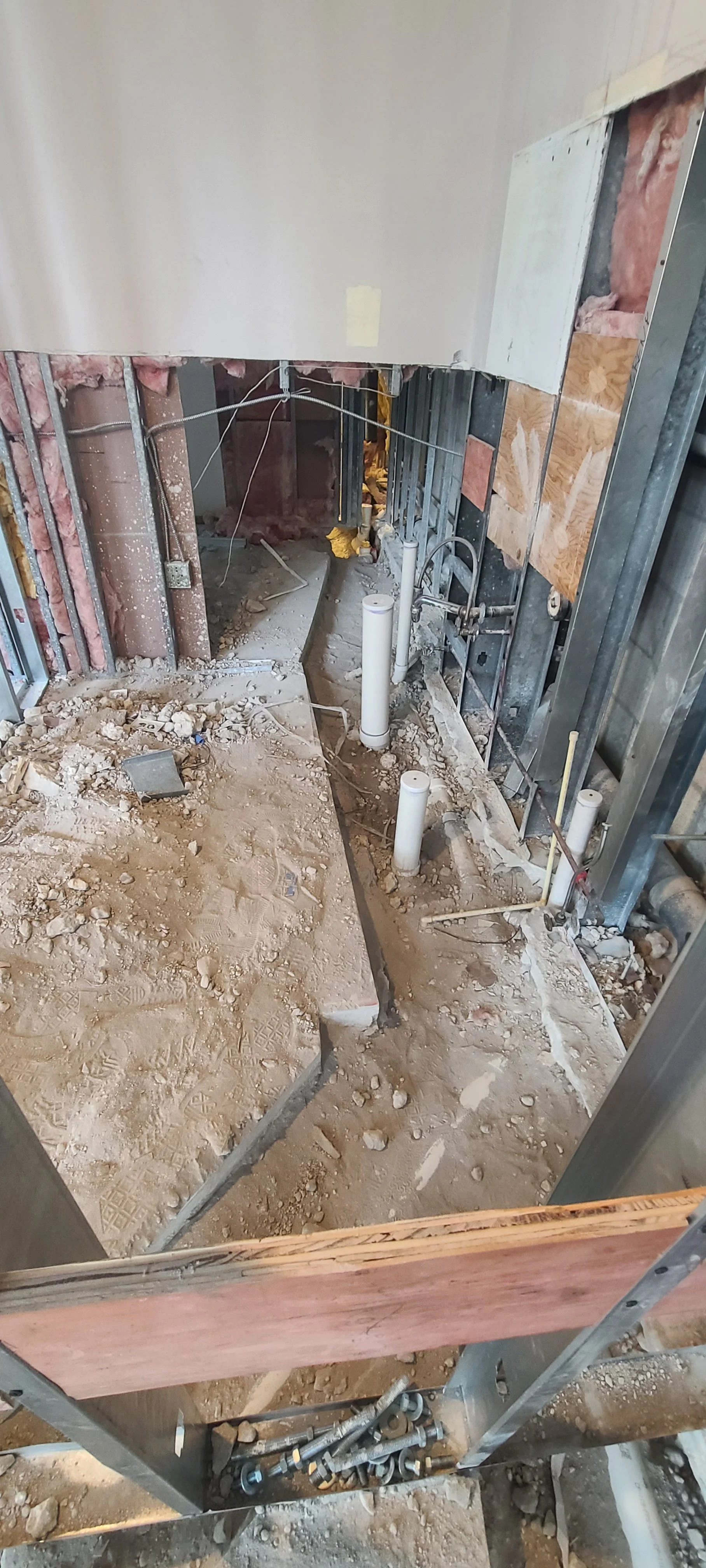 Undergoing bathroom renovation with exposed pipes, studs, and construction debris on the floor.