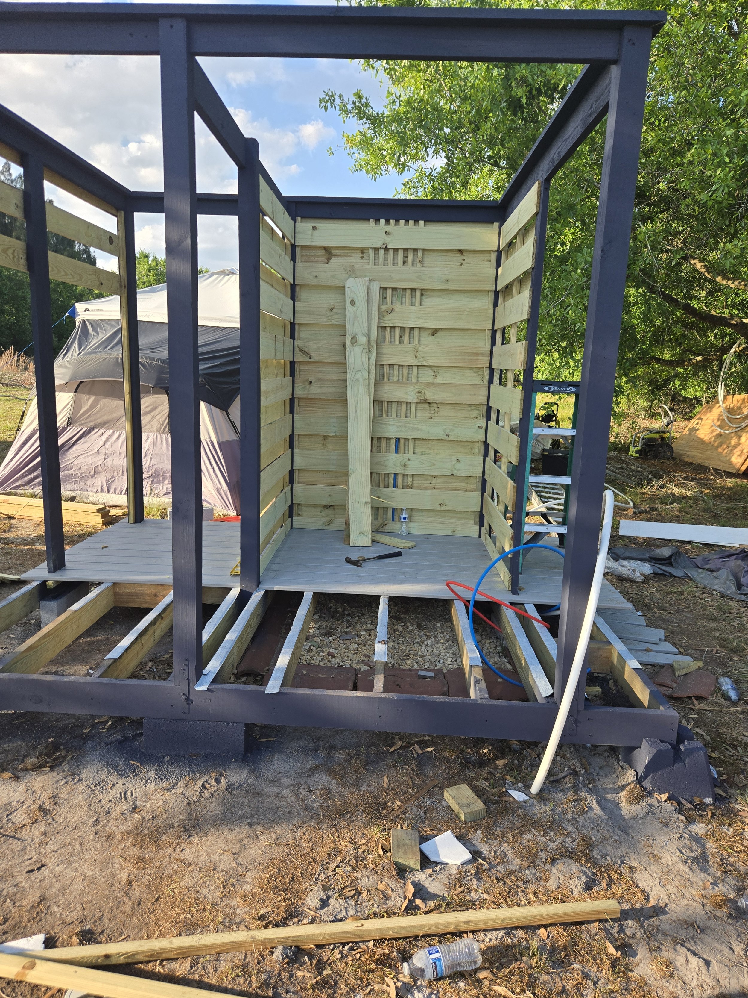Construction of an outdoor shed with a wooden interior and a metal frame, partially built, with construction tools and materials on site.