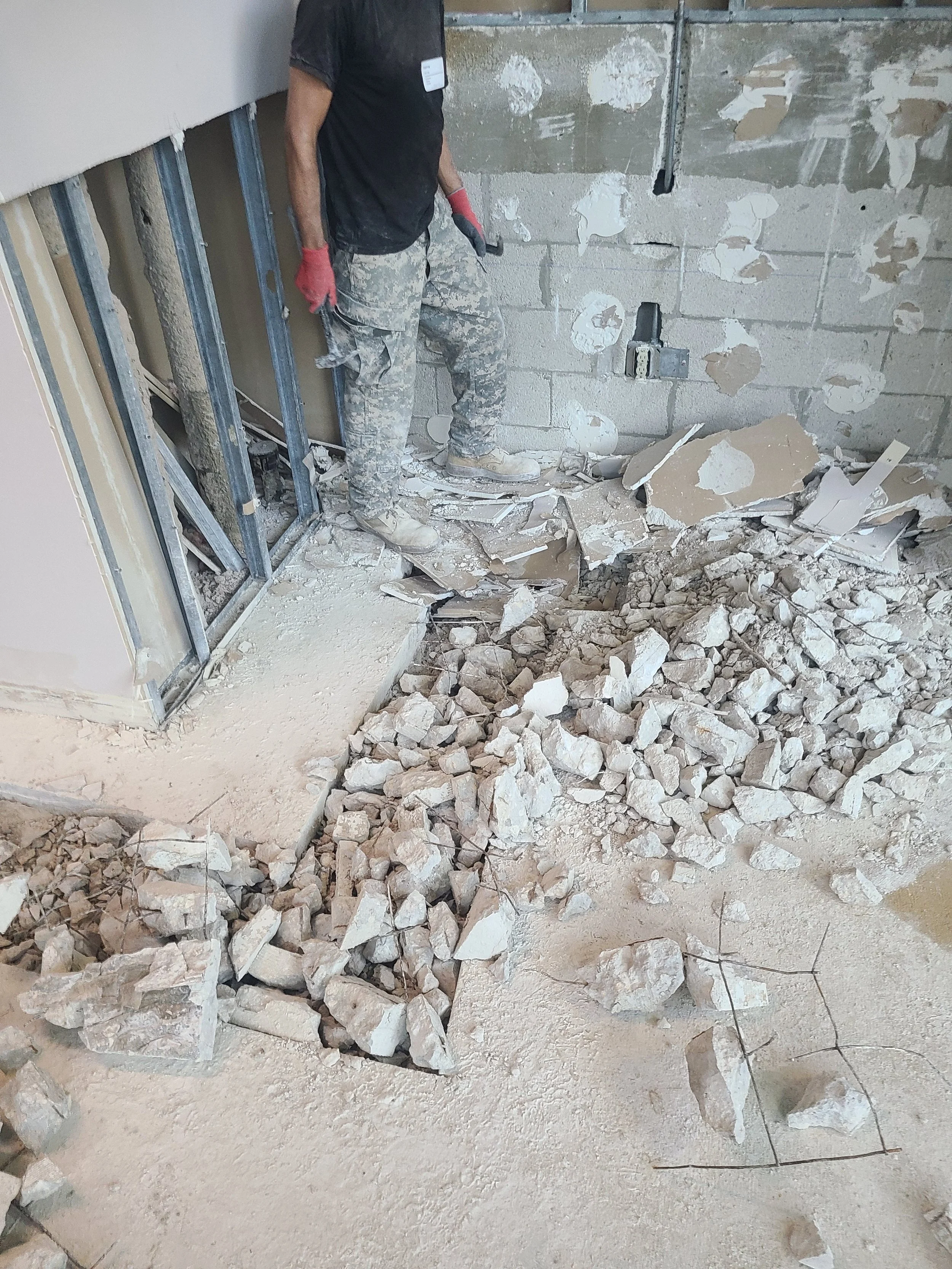 A worker breaking a concrete floor into rubble during an office renovation.