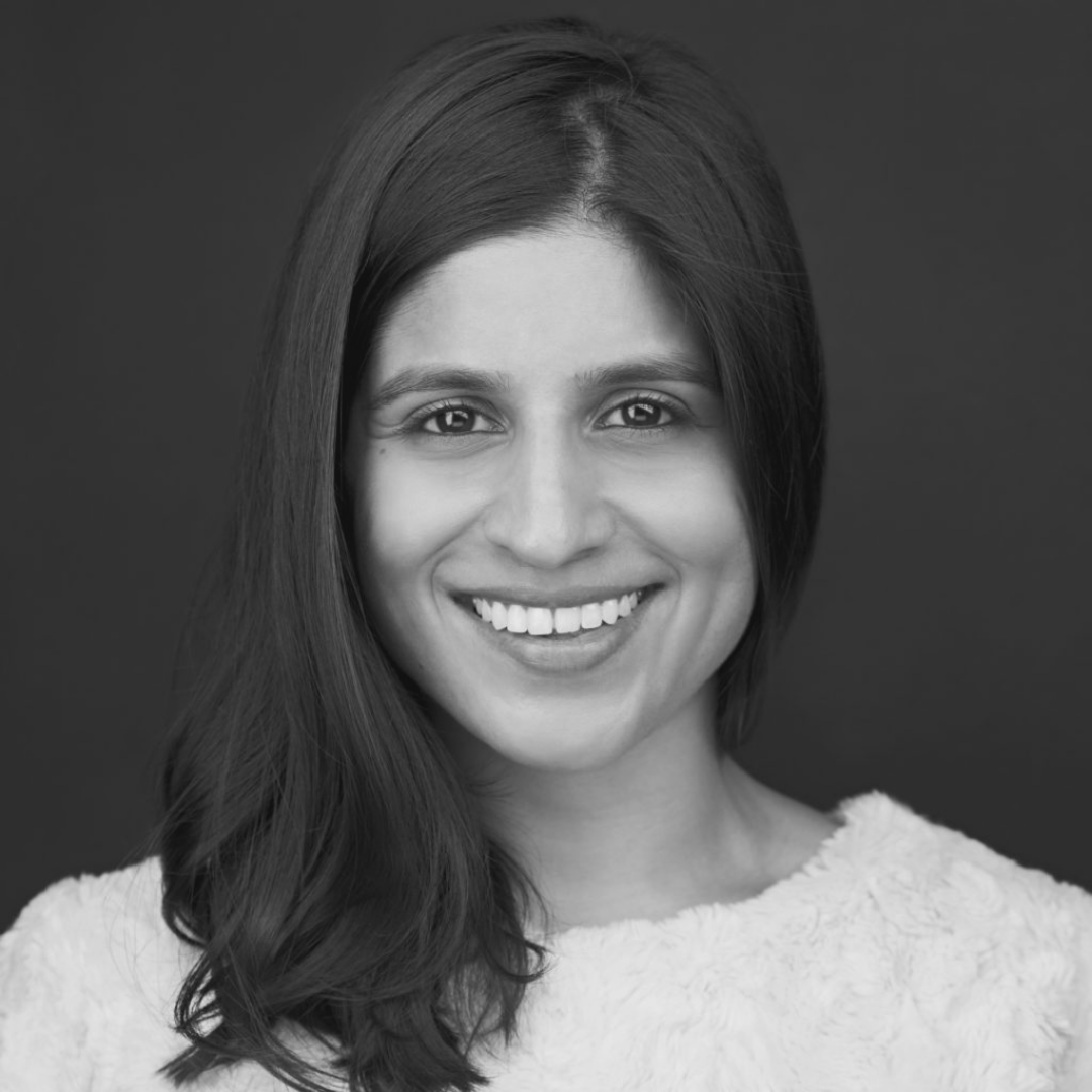 Black and white portrait of a smiling woman (Ashna Shah) with shoulder-length hair, wearing a light-colored textured top.