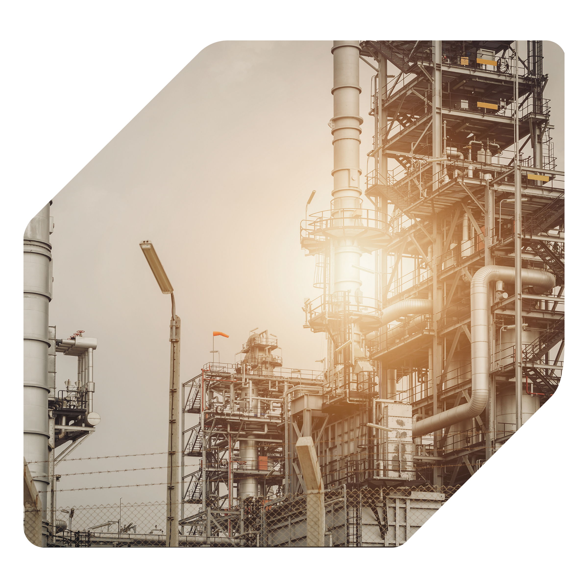 Industrial facility with multiple pipes, platforms, and metal structures, enclosed by a chain-link fence.