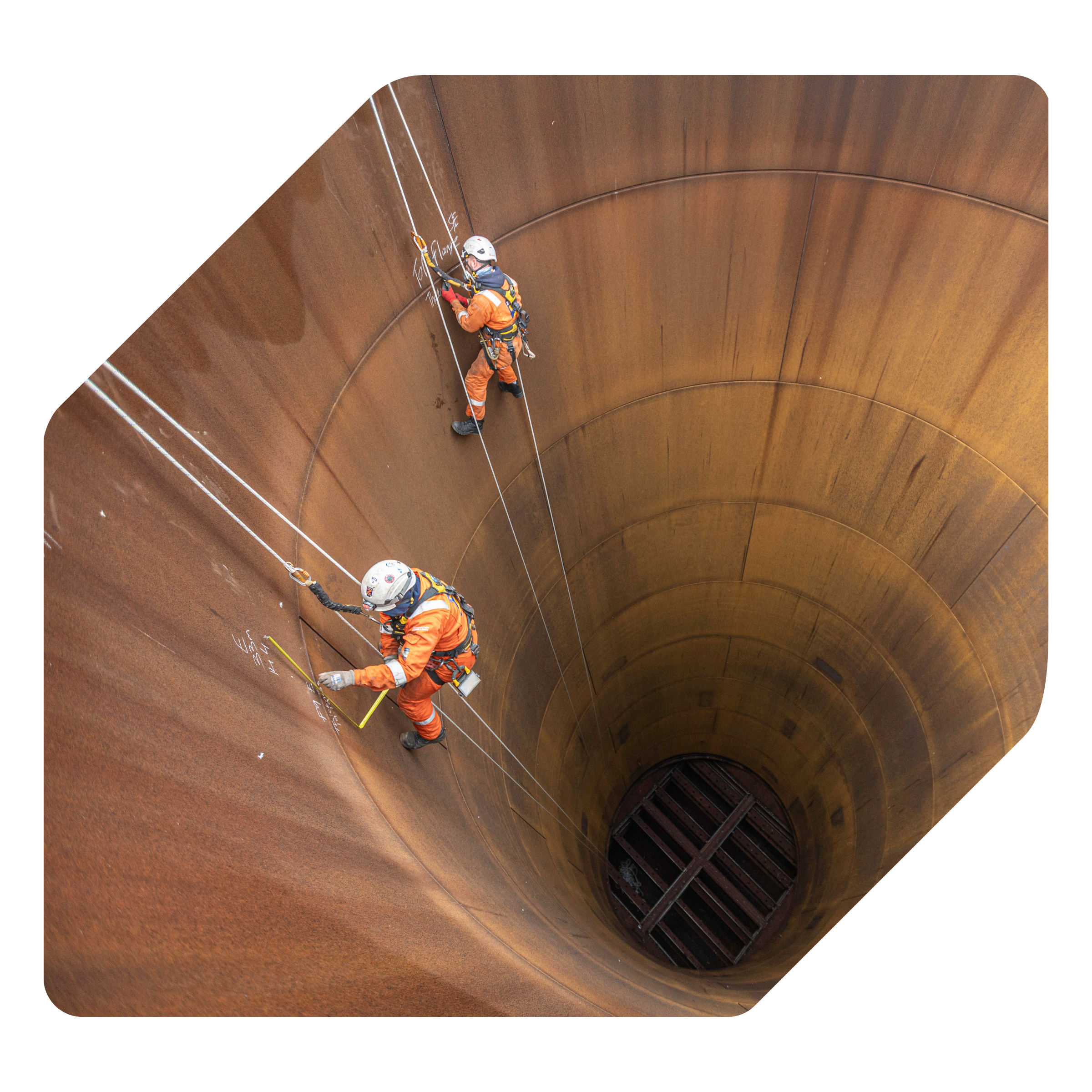 A worker wearing safety gear and climbing equipment inside a large, cylindrical metal structure.
