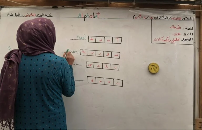 Syrian refugee woman writing on a board while practicing reading and writing during a literacy workshop for parents.