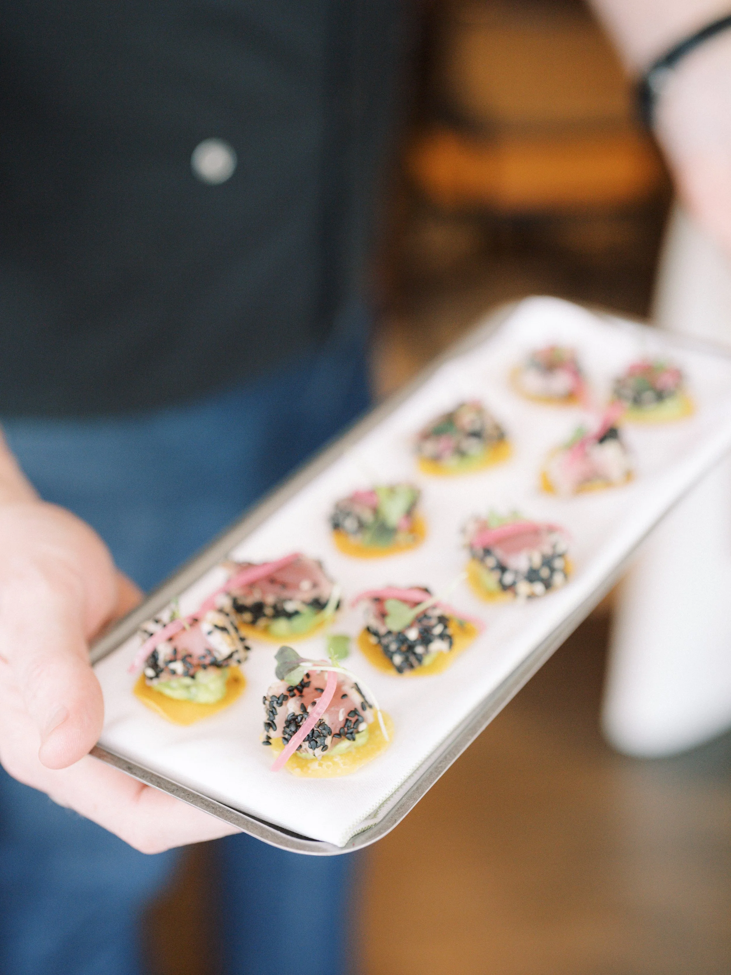 A person holding a tray of decorated appetizers with pink, black, and green toppings.