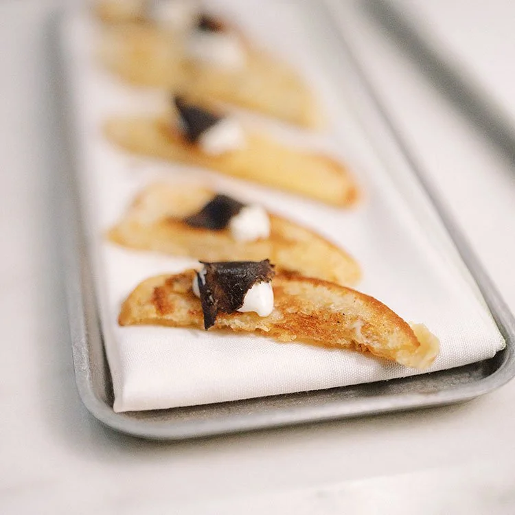Close-up of gourmet pierogis on a silver tray with a white cloth, topped with sour cream and a small piece of black caviar.