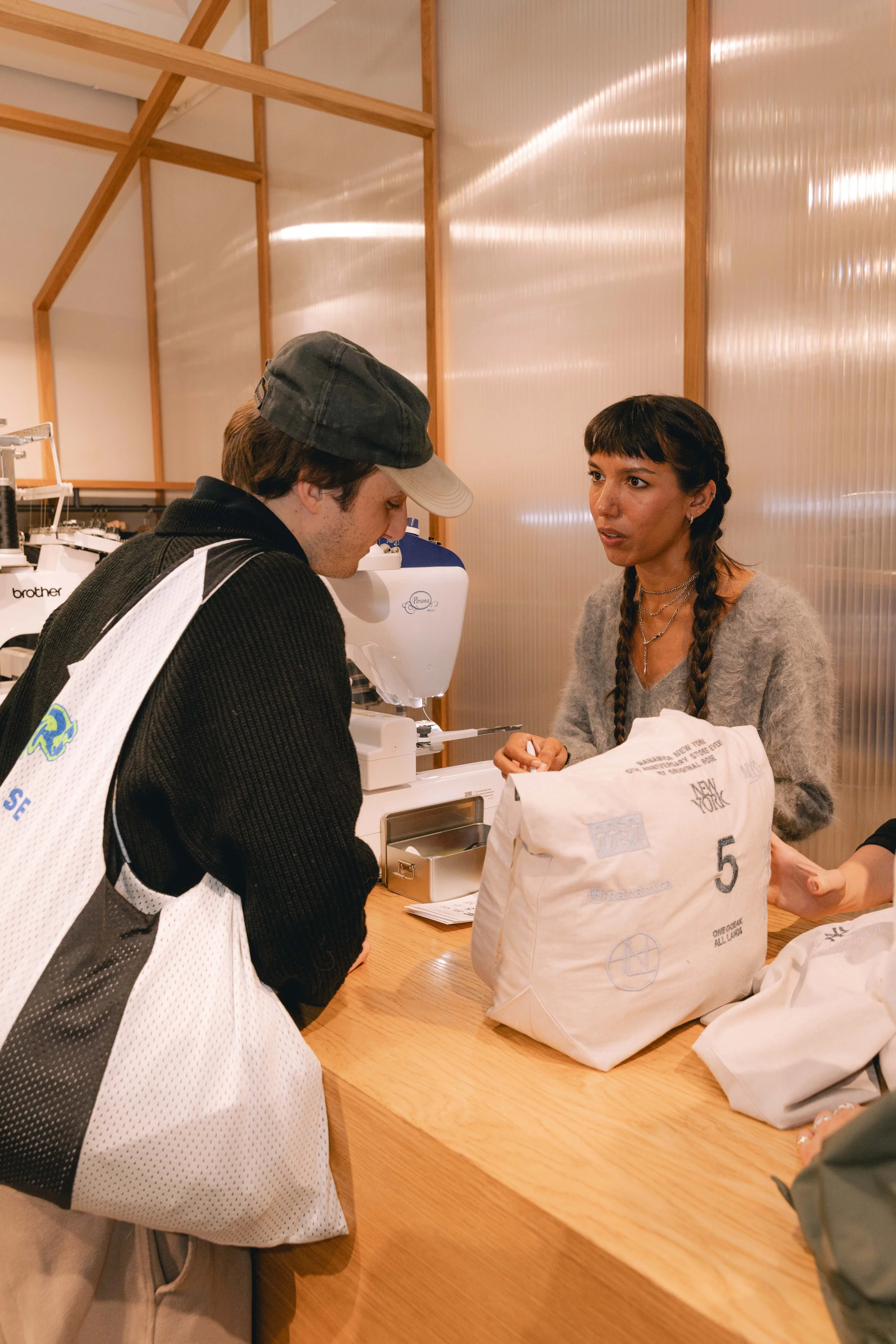 A man and a woman at a checkout counter, with the man paying with a card and the woman assisting, in a room with wood and metal panel walls.