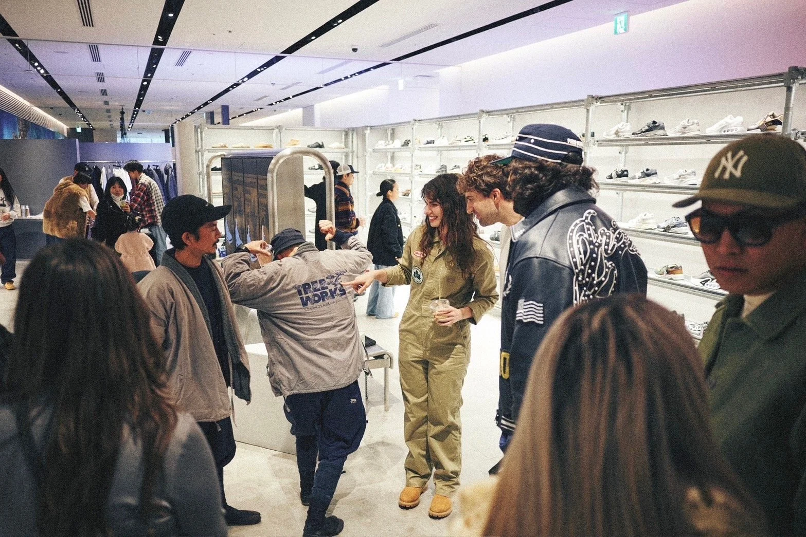 Group of people shopping and socializing inside a sneaker retail store, with shelves of sneakers on the wall in the background.