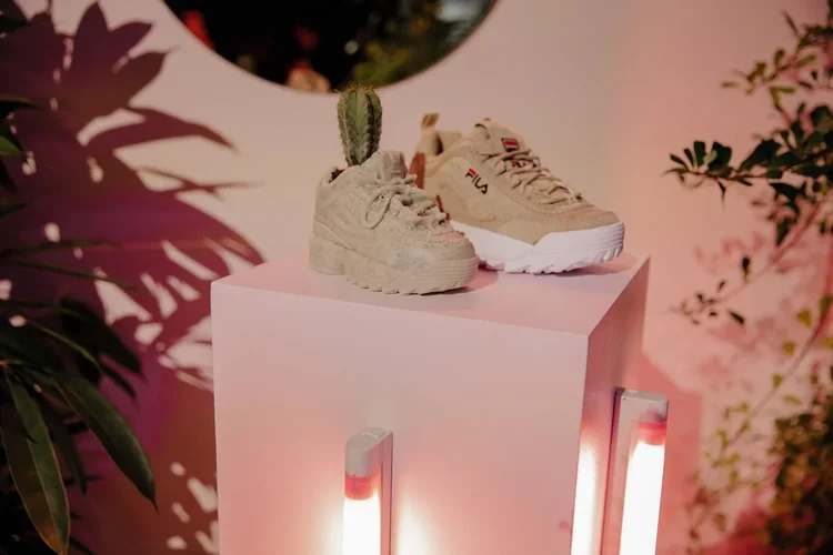 FILA Disruptor sneakers on a pink pedestal beside a cactus