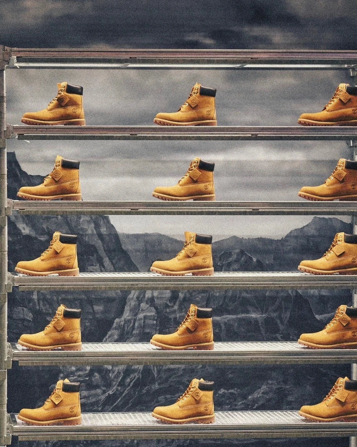 Multiple pairs of yellow Timberland-style boots displayed on metal shelves against a mountainous landscape with cloudy sky in the background.