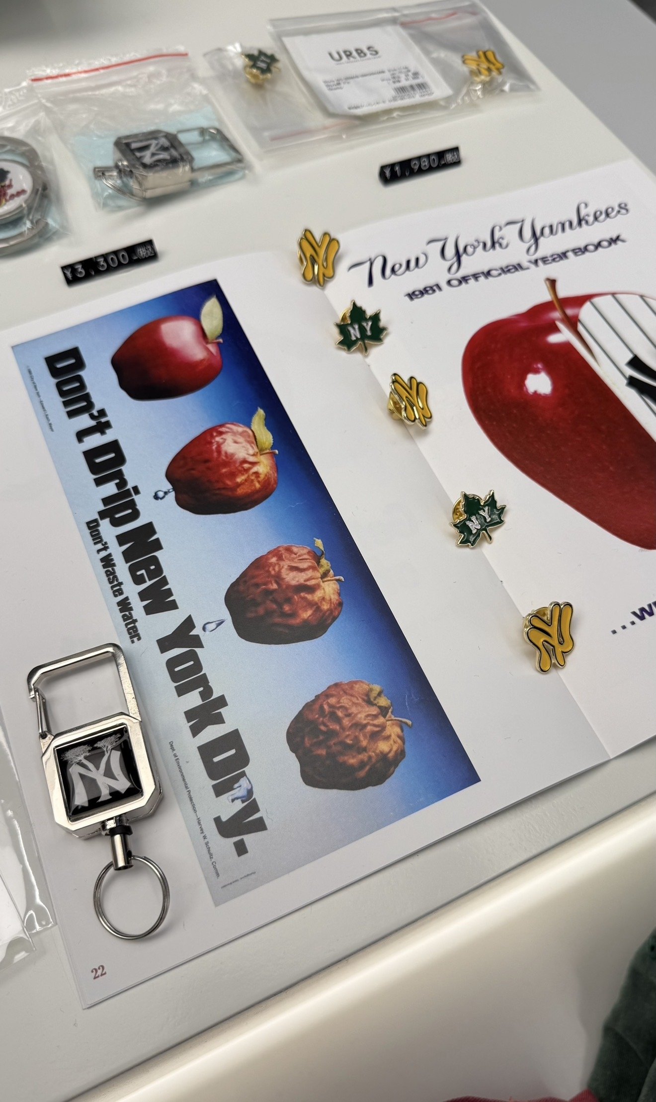 A collage of old Nancy Yankee memorabilia including pins, stickers, a keychain, and a newspaper clipping showing apples, with a sign that says "Don't Dnap New York" and the text "New York Yankees 1991 Official Yearbook."