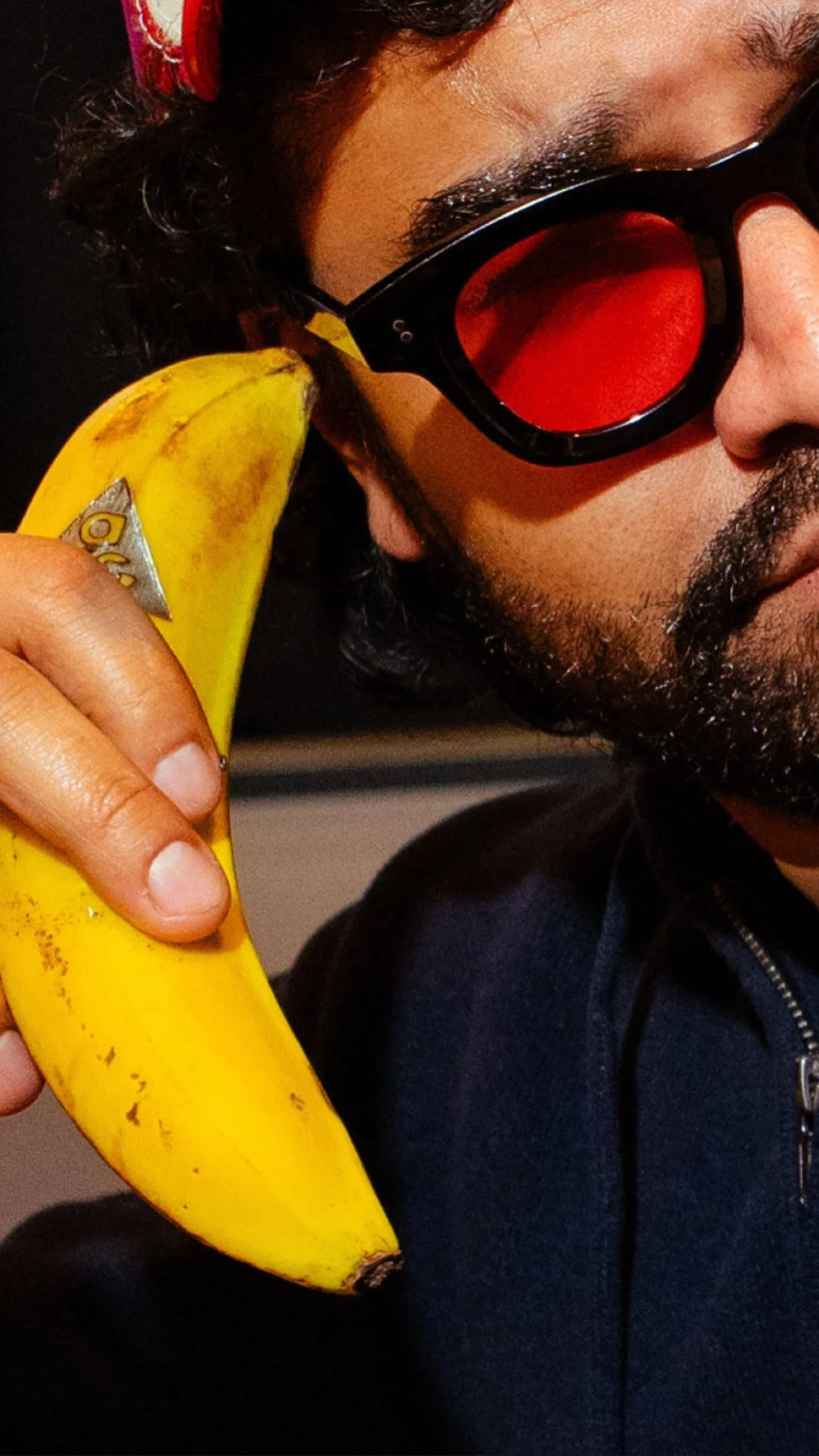 Person with dark sunglasses holding a banana close to their head in a phone-like pose.