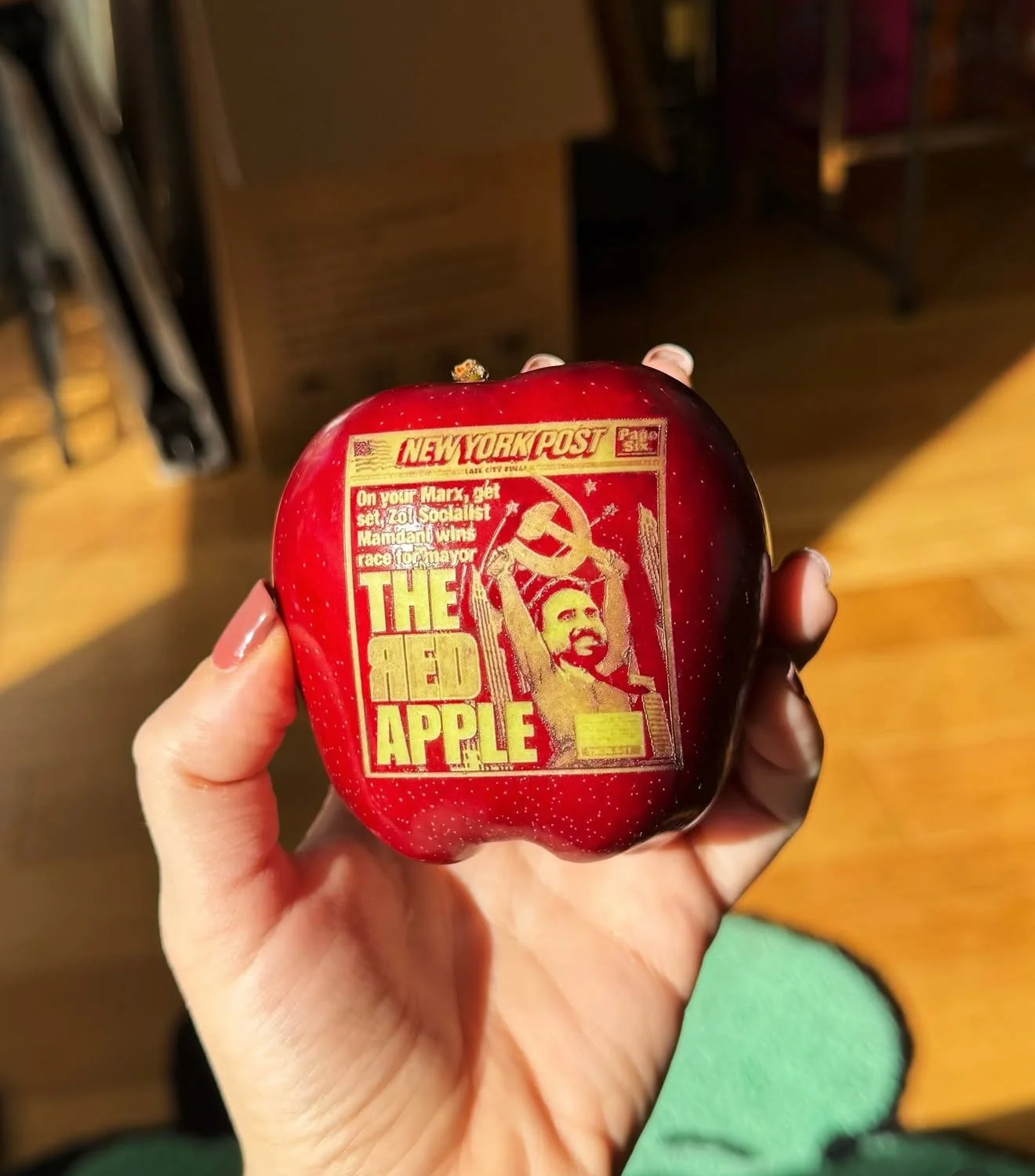 A red apple with a cover of a vintage New York Post newspaper featuring a caricature of a person holding a hammer, with the headline 'The Red Apple'.