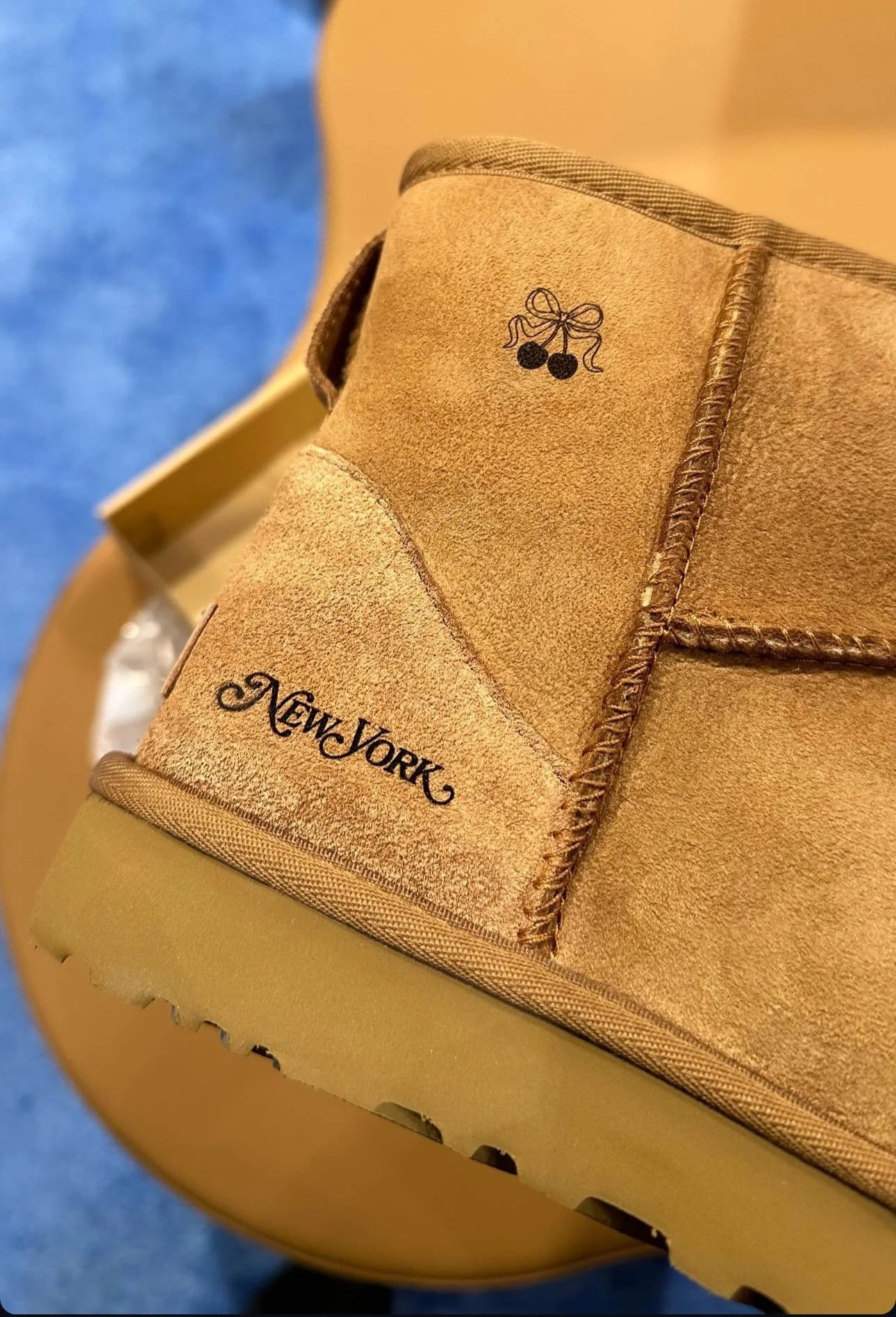 Brown suede boot with embroidery of a bow and cherries, and the words "New York" stitched on the heel.