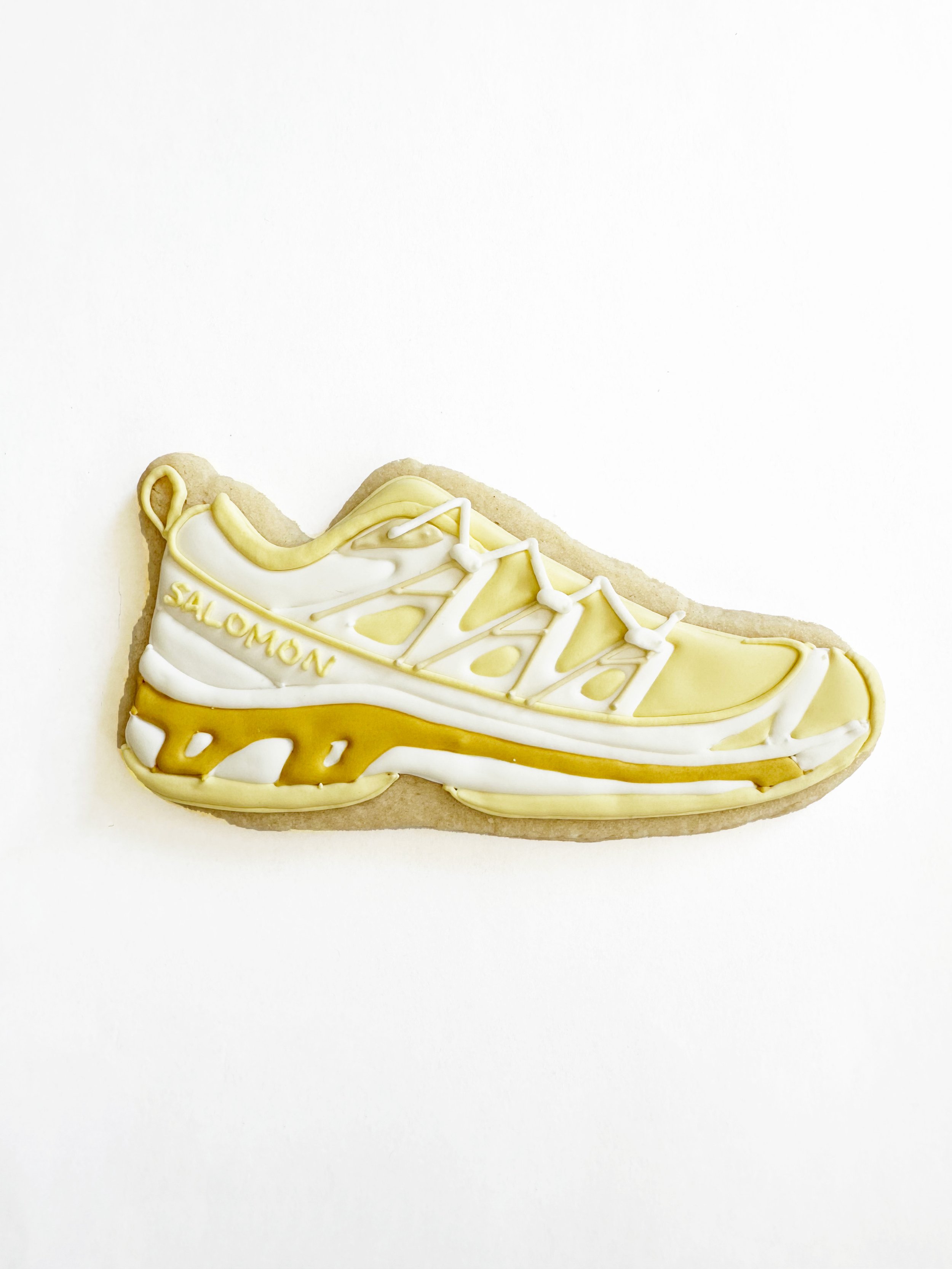 A cookie shaped like a Salomon running shoe, decorated with yellow and white icing.