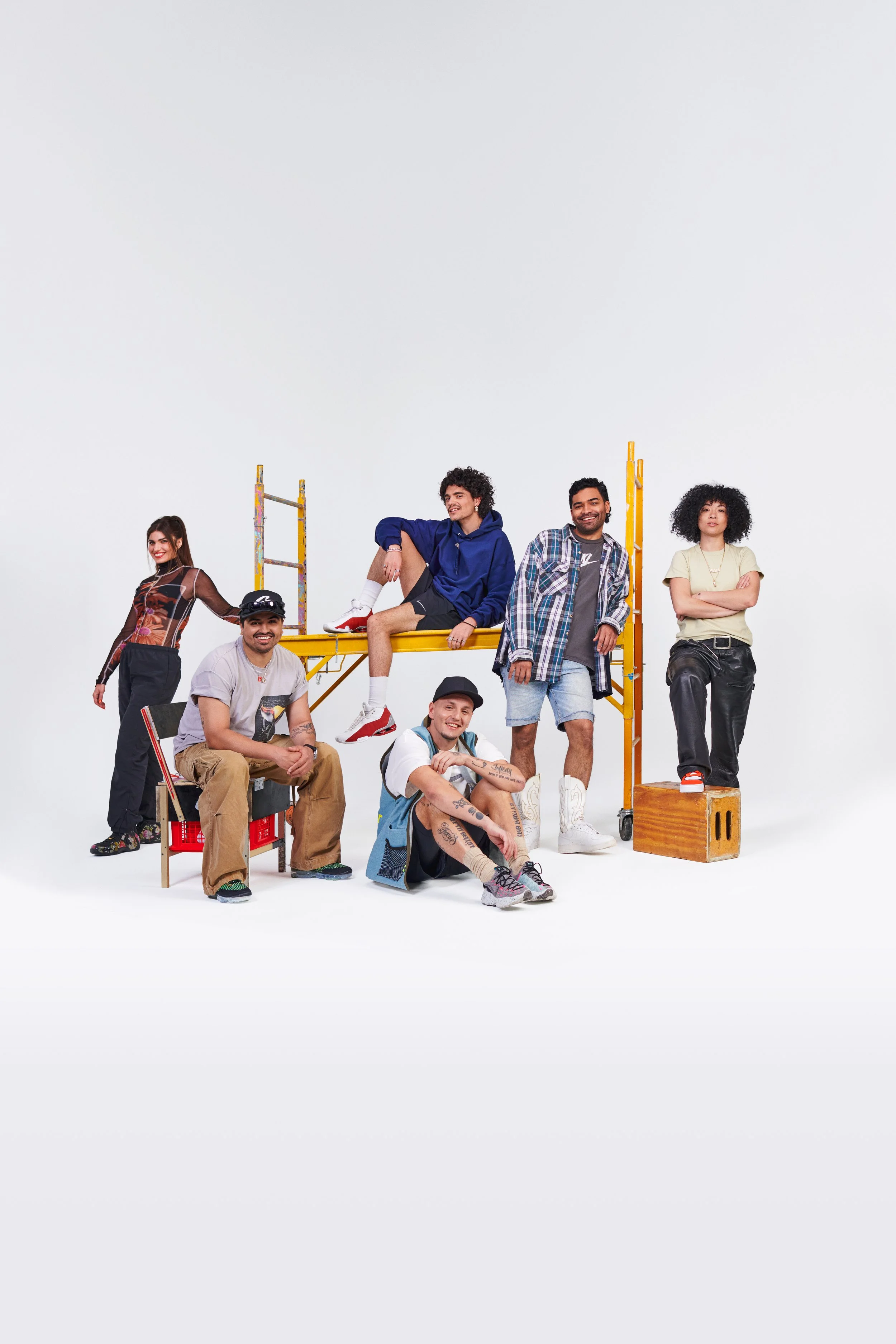 Group of seven diverse young people posing with workout equipment and casual clothes against a white background.