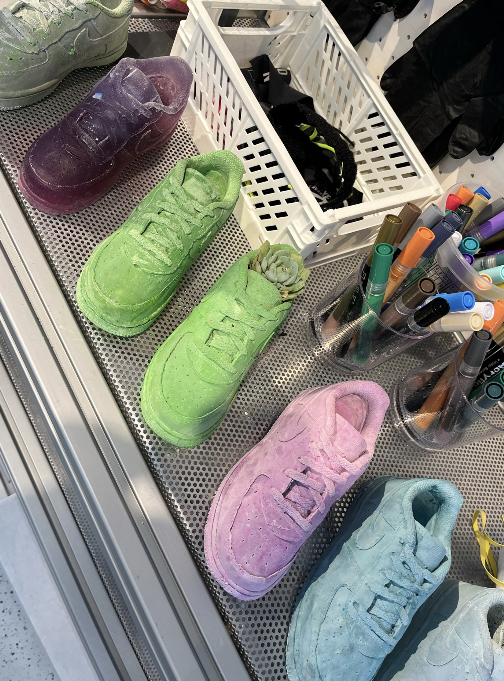Colorful sneakers in purple, green, pink, and blue on a metal surface, with markers and miscellaneous items nearby.