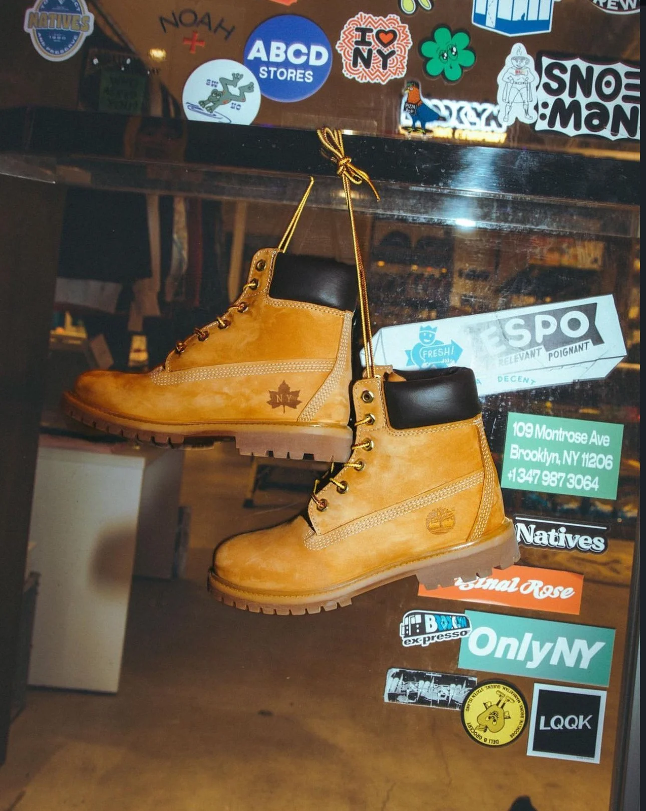 A pair of tan Timberland-style boots hanging in a store, surrounded by various colorful stickers on the glass, including store addresses, logos, and design elements.