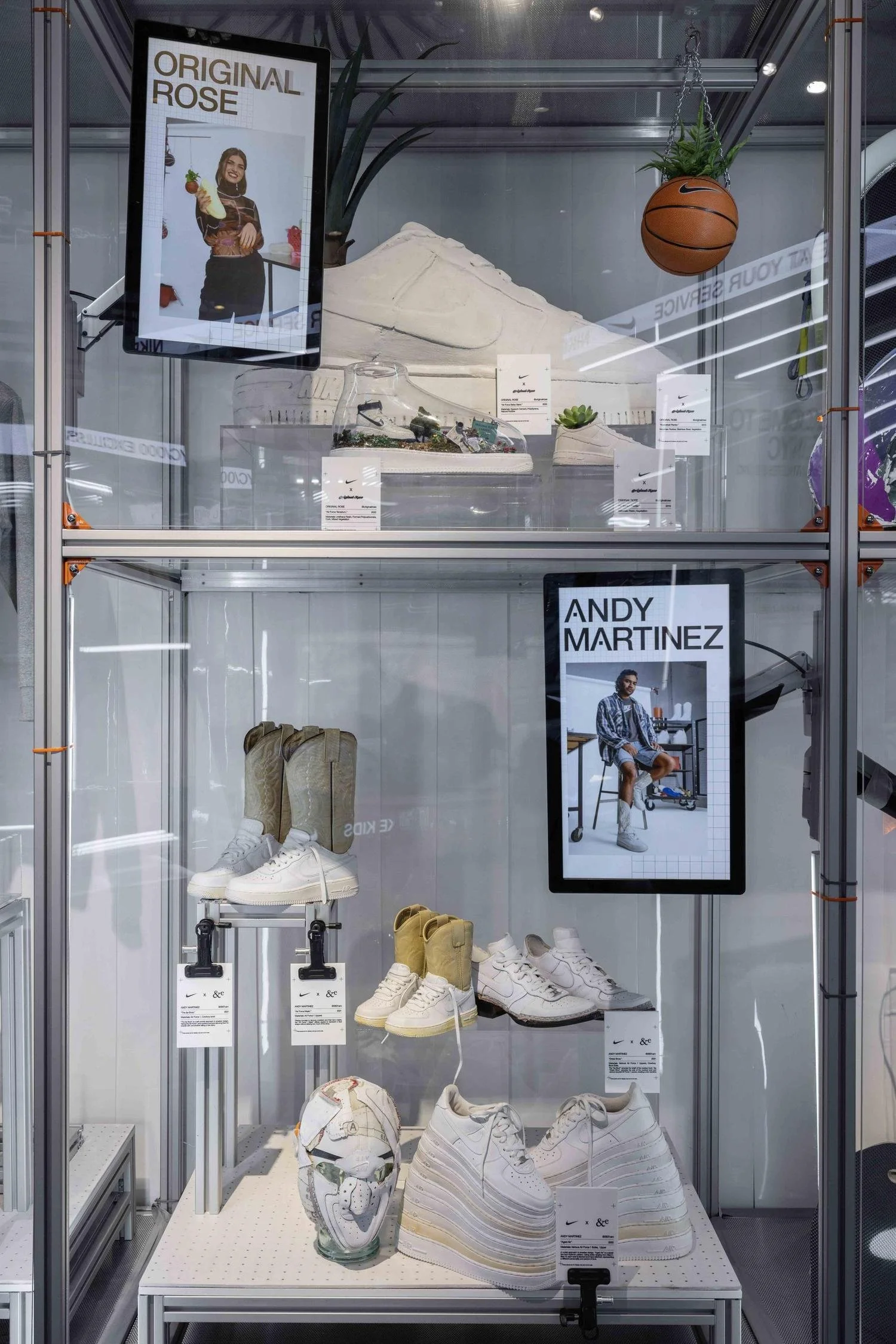 Display case featuring Nike shoes, a pair of beige boots, and an artistic mask, with posters of models and a basketball hanging above.