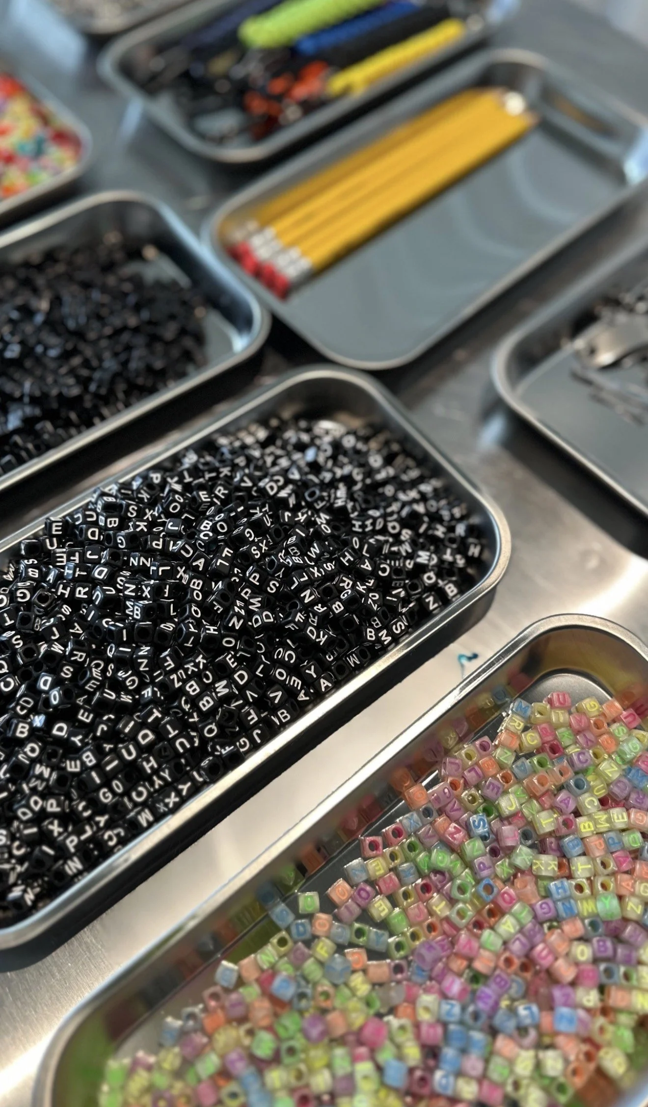 Close-up of various containers of small colorful alphabet beads and lettered jewelry-making supplies on a table.