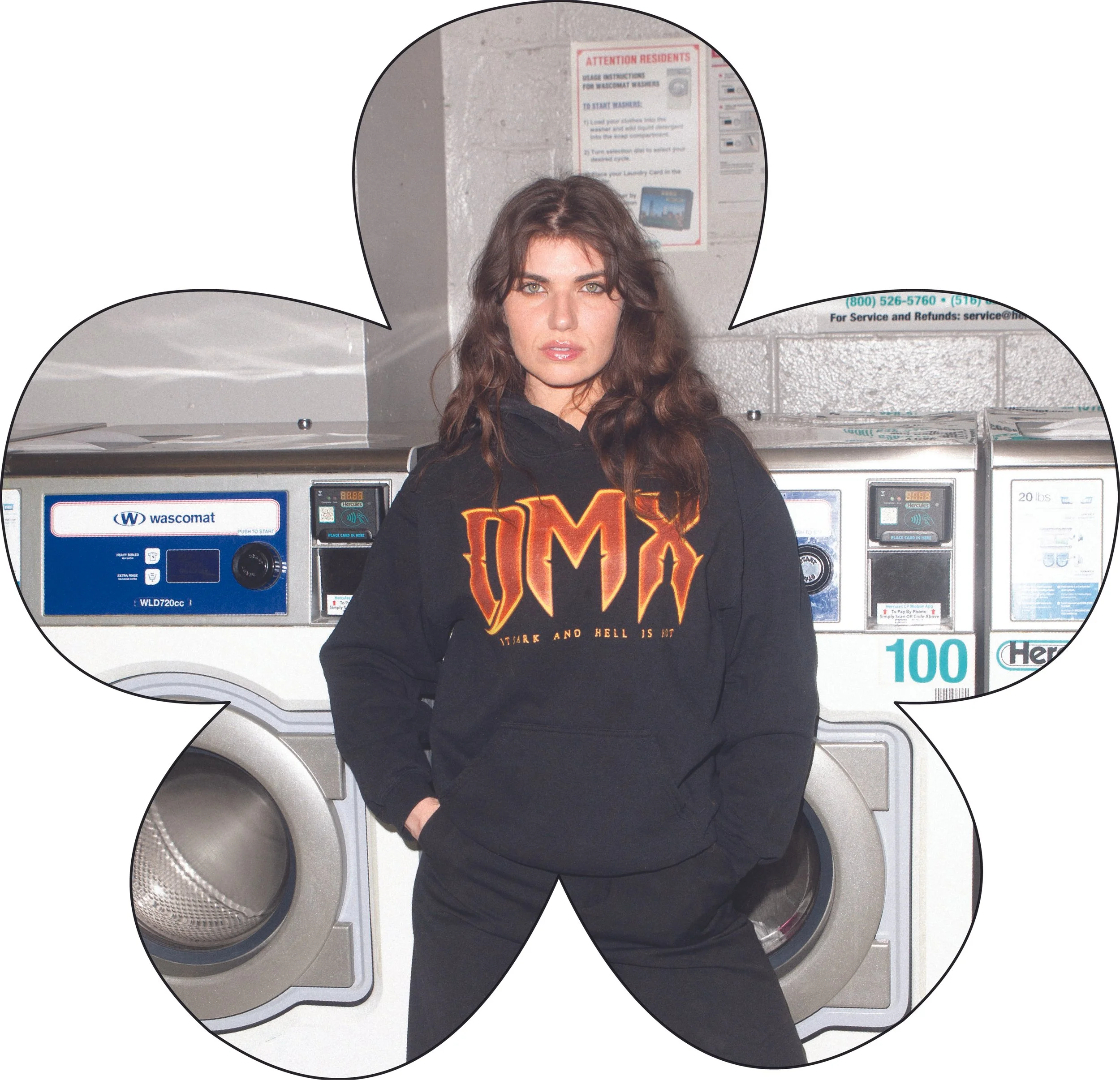A woman with long, wavy brown hair and light skin standing in front of a laundromat washing machine, wearing a black hoodie with orange and red text reading 'OMX' and 'STARK AND HELL IS NOT'.