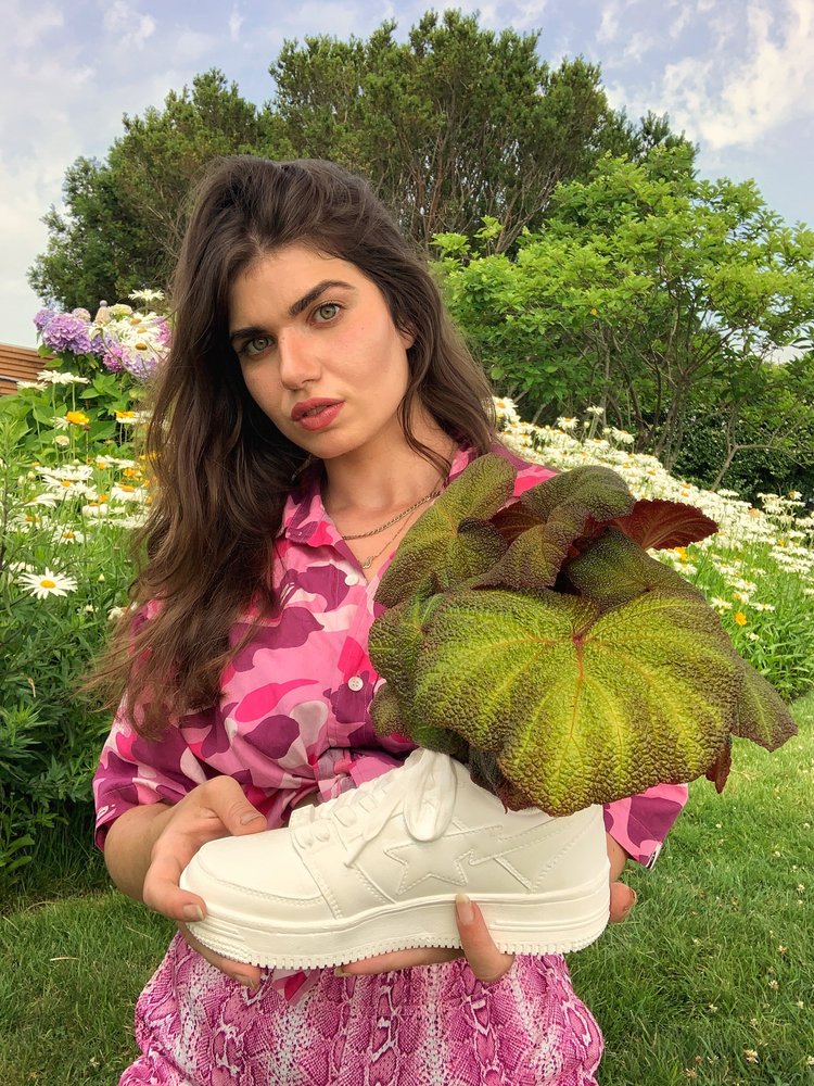 Holding the BAPE STA ceramic planter with leafy plants in a garden