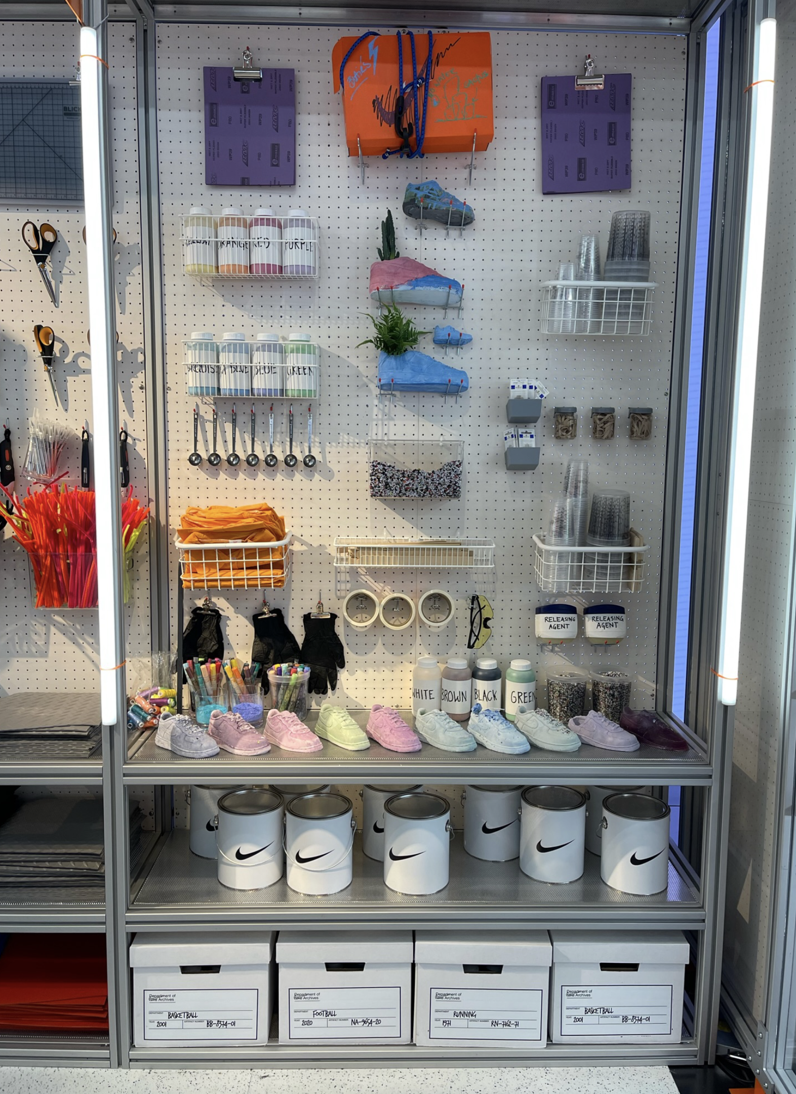 A display of sports and recreation supplies including colorful sneakers, spray paint, tape, cups, markers, scissors, and other items in a well-organized locker or storage unit.