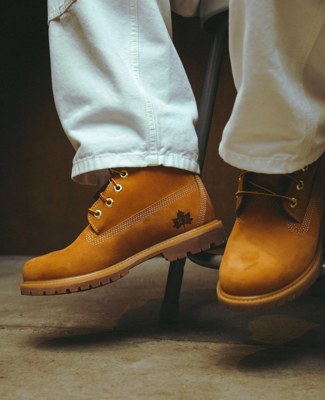 Close-up of a person wearing tan Timberland boots and white pants, with one foot slightly lifted off the ground, on a desk chair.
