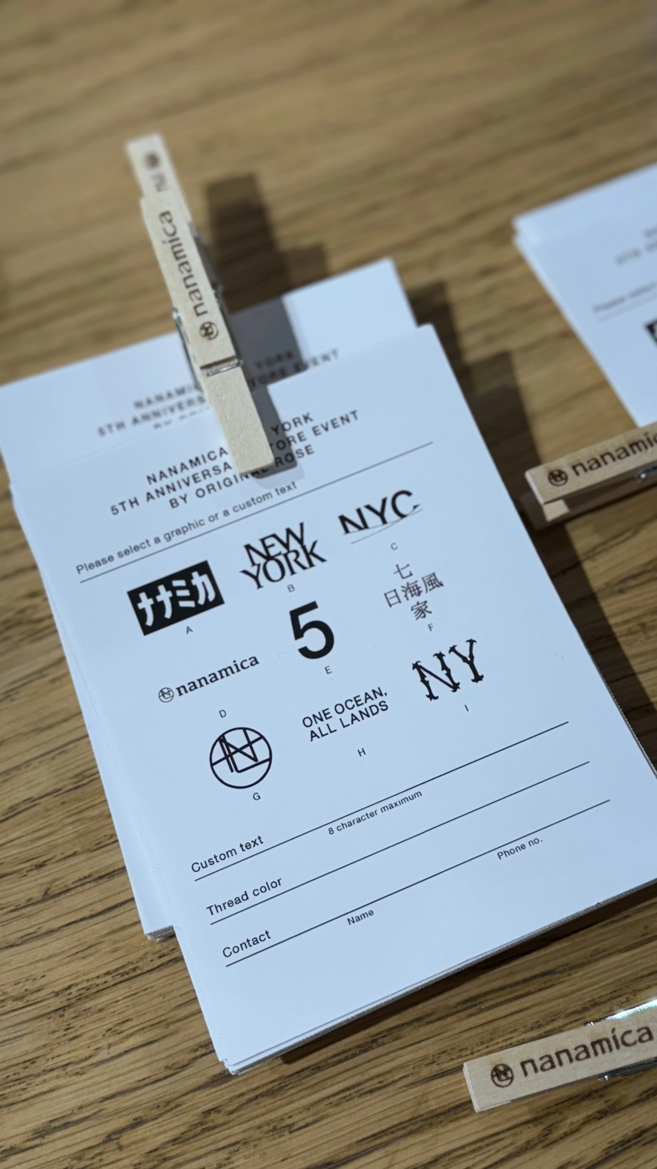 A ticket for Nanamica's 5th anniversary event in New York City, featuring various graphics, texts, and a wooden clothespin.