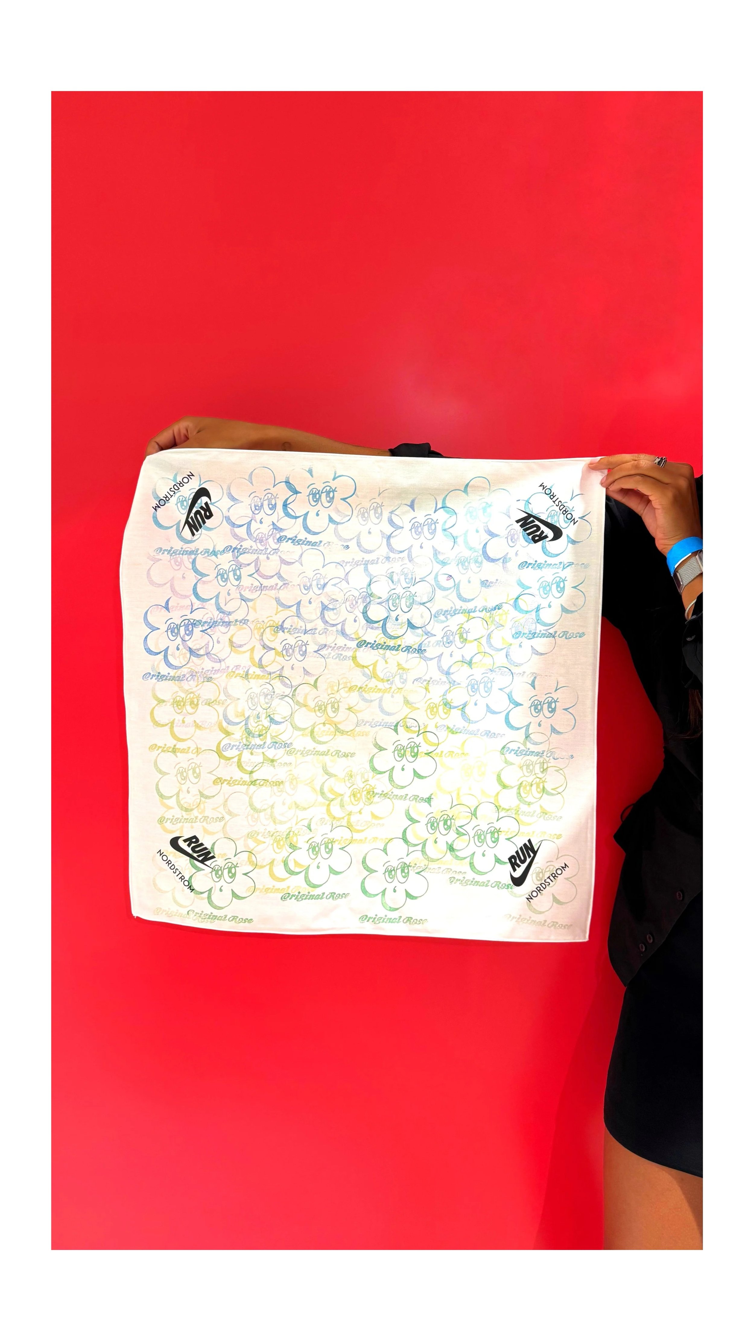 Person holding a white sheet with repeated colorful floral designs that have smiling faces, against a red background.