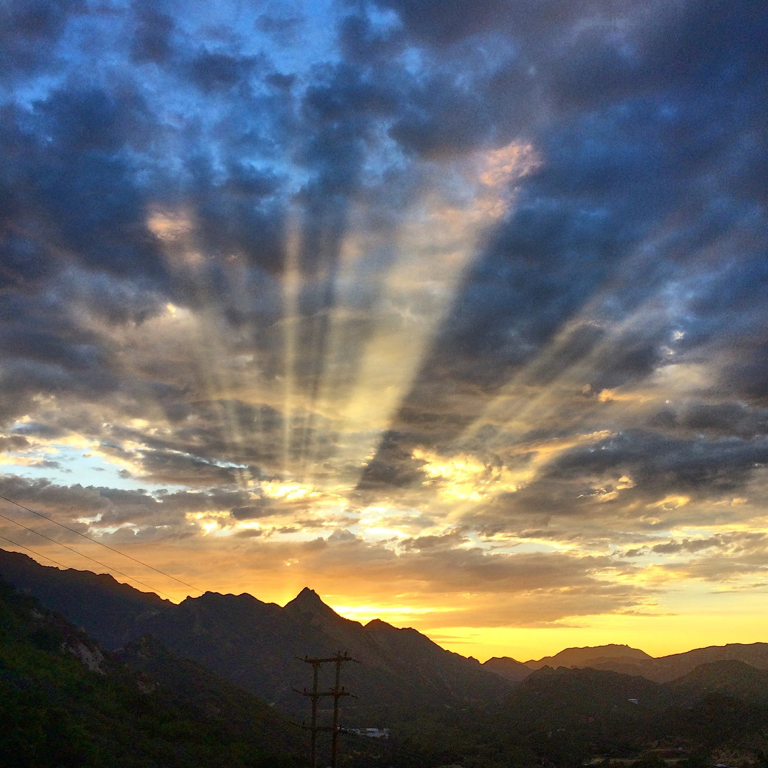 Sunset over mountain range with dramatic cloud sky and sun rays shining through.
