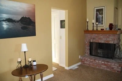 Living room with a brick fireplace, a framed photo above it, a small table with candles, and a wall art of a sunset over rocky shore.