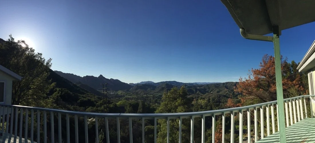 View from a balcony overlooking a mountainous landscape with trees and clear sky.