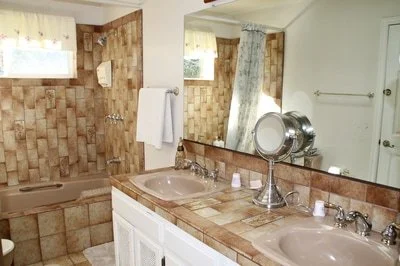 Bathroom with double sinks, mirror, and a bathtub with tiled walls in the background.