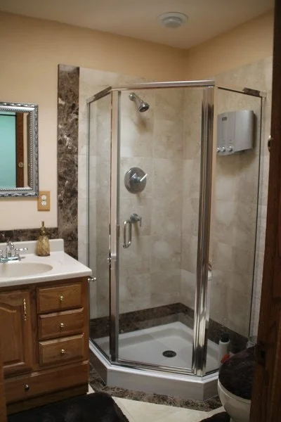 Bathroom with a corner glass shower enclosure, a wooden vanity with a white countertop, a soap dispenser, and a mirror with a decorative frame.