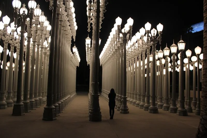 A person standing under an art installation of numerous illuminated street lamps at night.