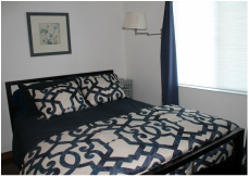 A neatly made bed with black and white patterned bedding in a room with a window and blue curtains.